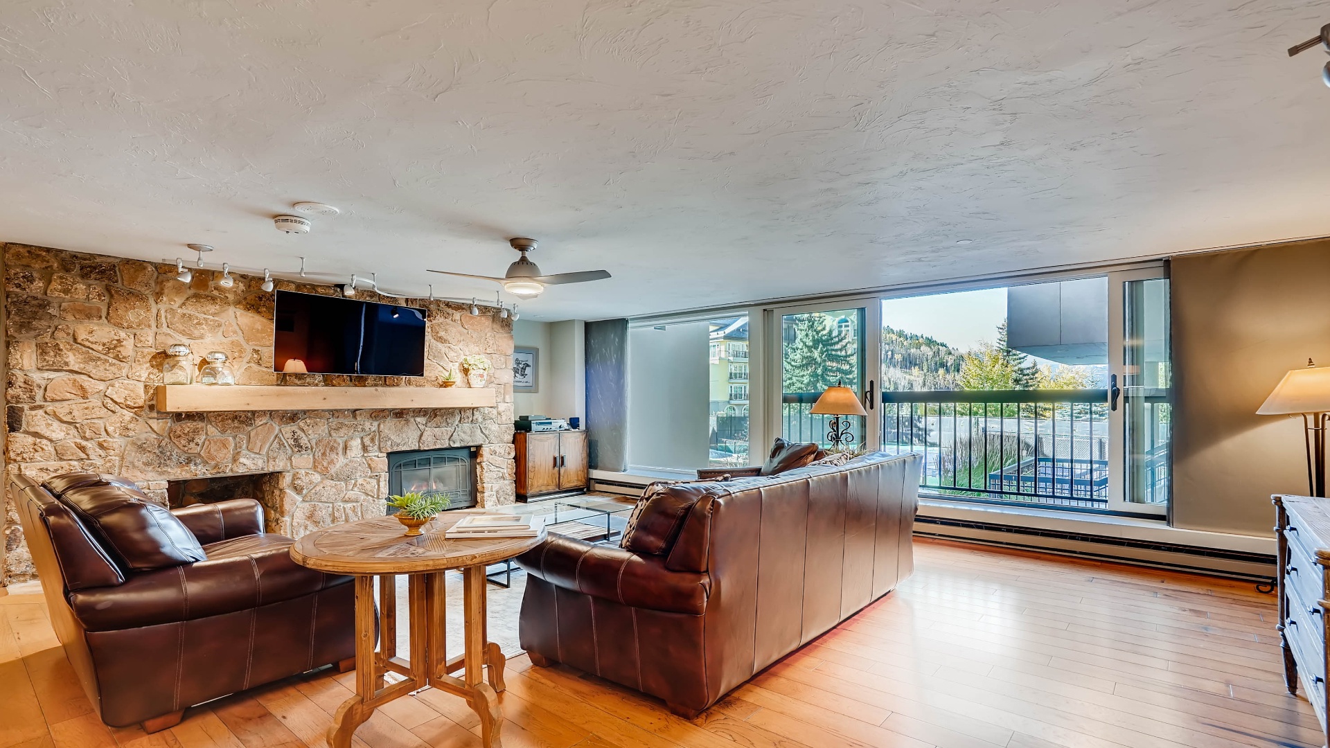 Relax in your spacious living room featuring a cozy stone fireplace, plush leather seating, and expansive windows framing beautiful mountain views—your perfect retreat after a day of adventure.
