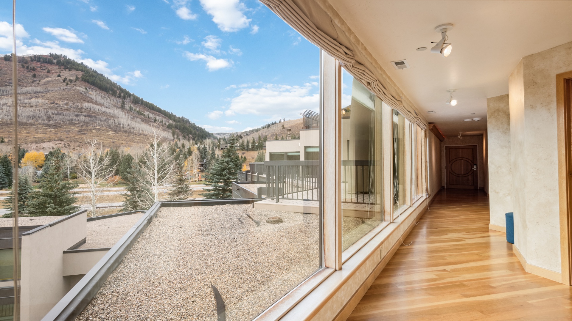 A bright hallway framed by expansive windows offering stunning mountain scenery with evergreen forests and golden foliage—creating a welcoming entryway with natural light and alpine charm year-round.