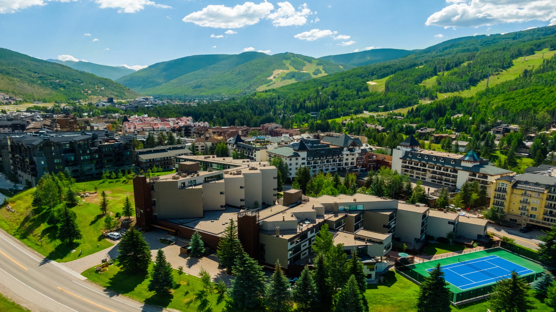 Aerial view of the property nestled in a mountain resort town, surrounded by lush green slopes, ski trails, and expansive natural landscape.