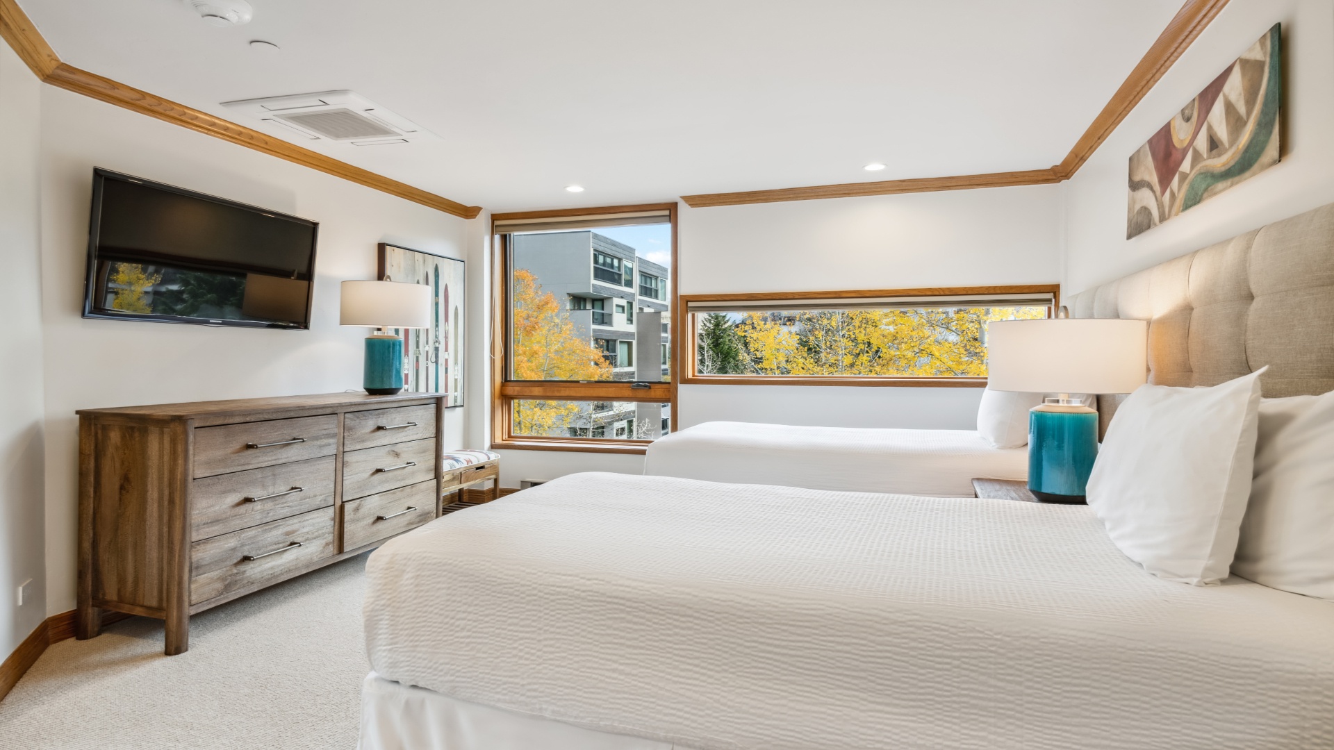 Wake up to crisp white linens and vibrant autumn foliage framed perfectly by your bedroom windows, where modern comfort meets natural beauty in every detail.