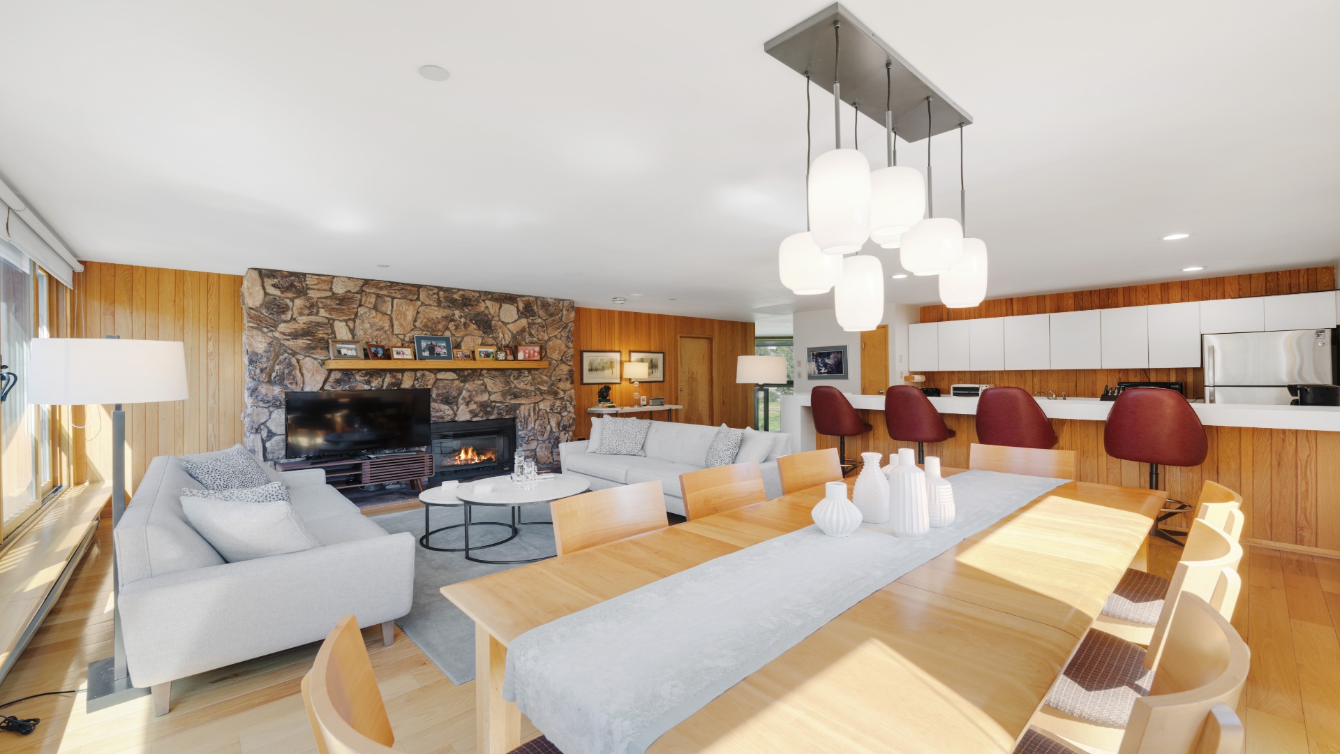 Relax in your open-concept living space featuring a cozy stone fireplace, modern entertainment center, and stylish dining area bathed in natural light—perfect for memorable gatherings.