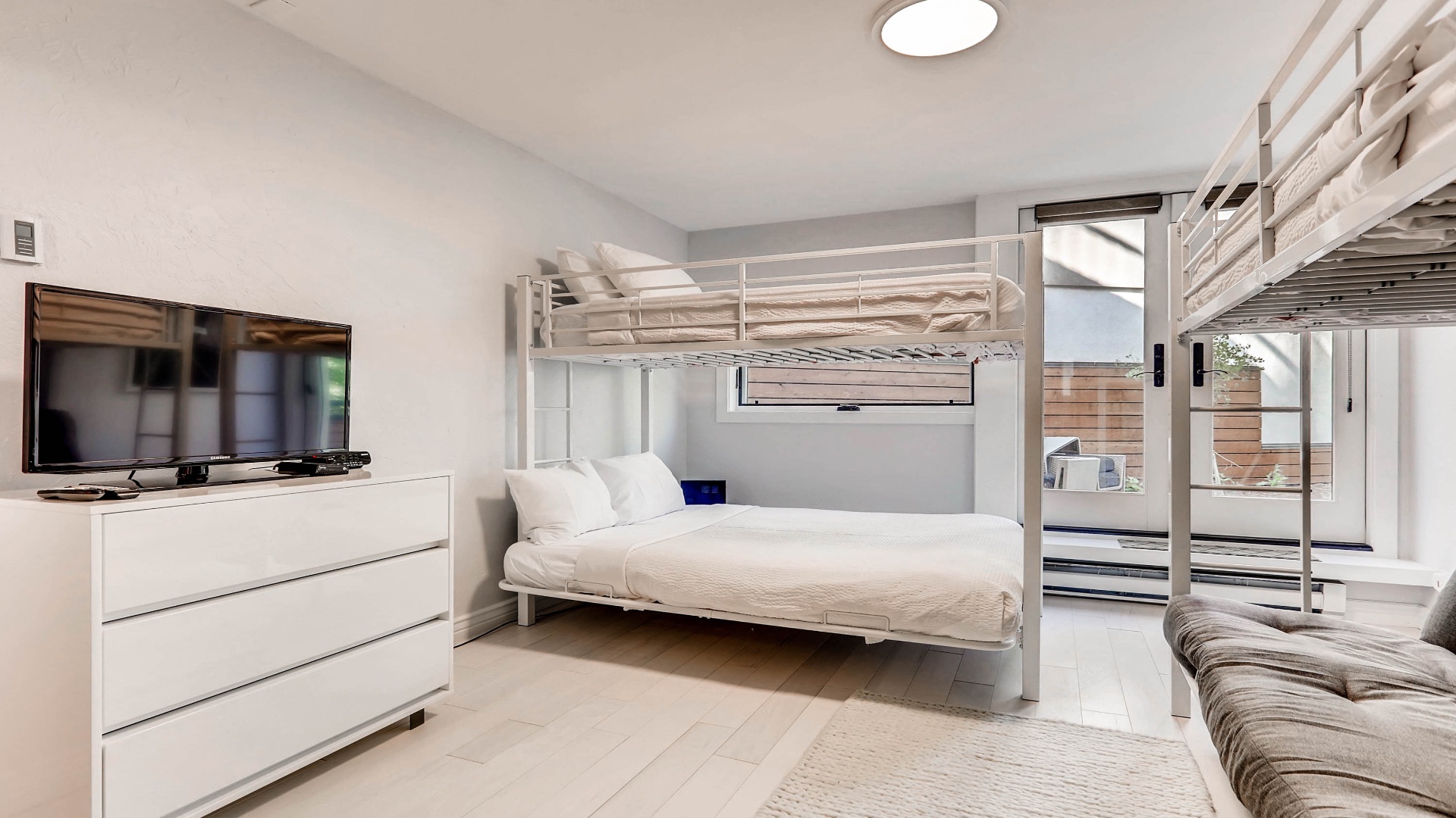 Your bright, modern bedroom features stylish bunk beds and a cozy sofa, perfect for families or groups seeking comfortable accommodations with direct patio access.