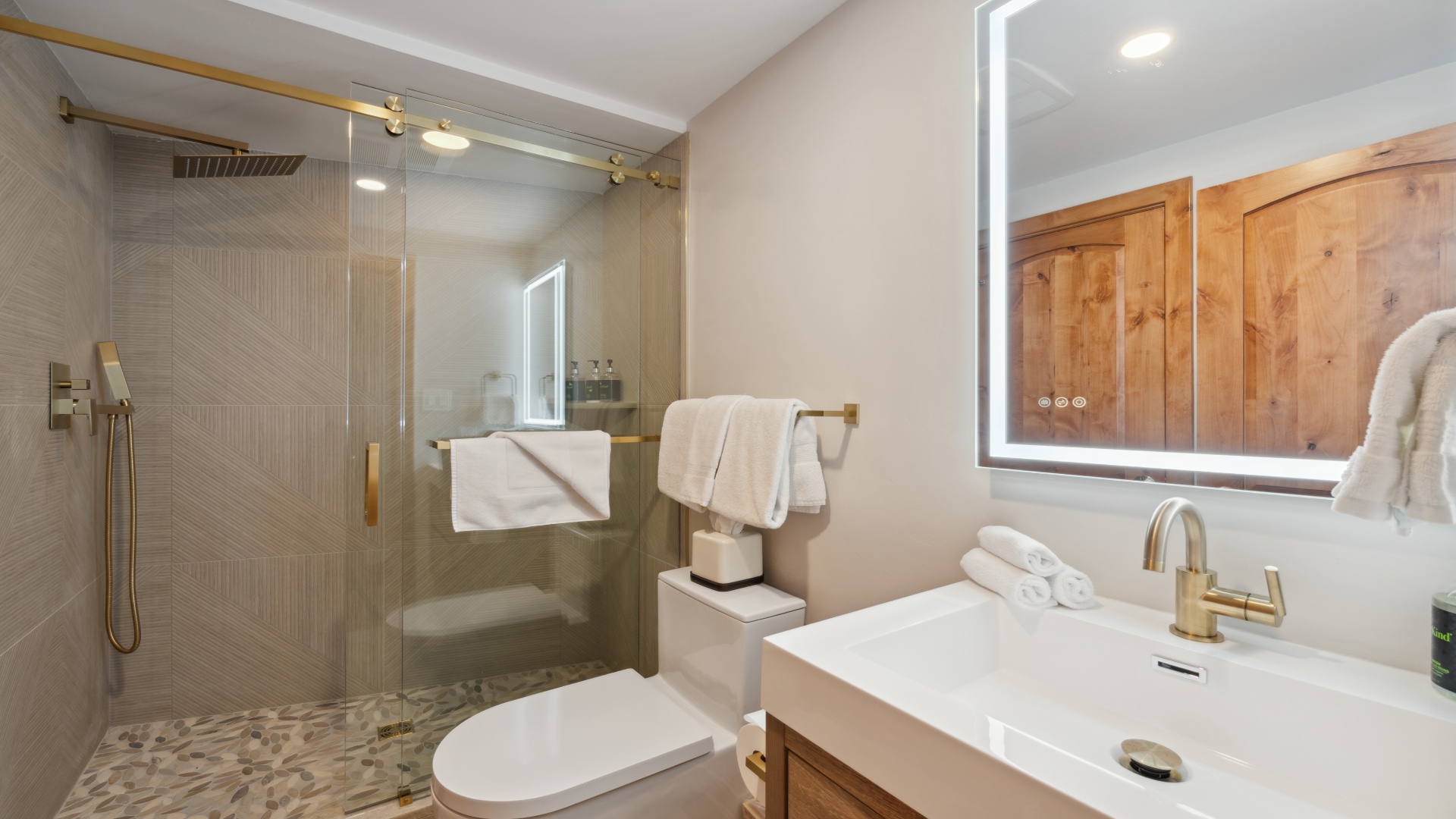 Step into your private spa-like retreat featuring a spacious walk-in shower with elegant gold fixtures, warm wood accents, and soft lighting that creates the perfect ambiance for unwinding after a day of adventure.