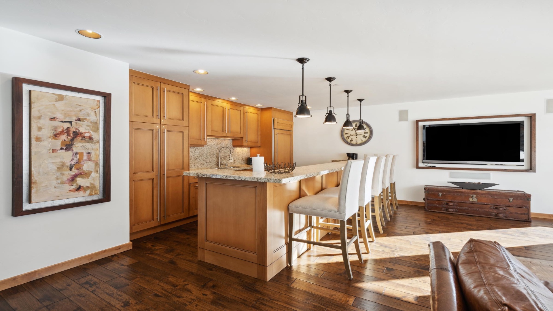 Settle into your open-concept living space featuring a chef's kitchen with warm wood cabinetry, granite counters, breakfast bar, and flat-screen for cozy gatherings.