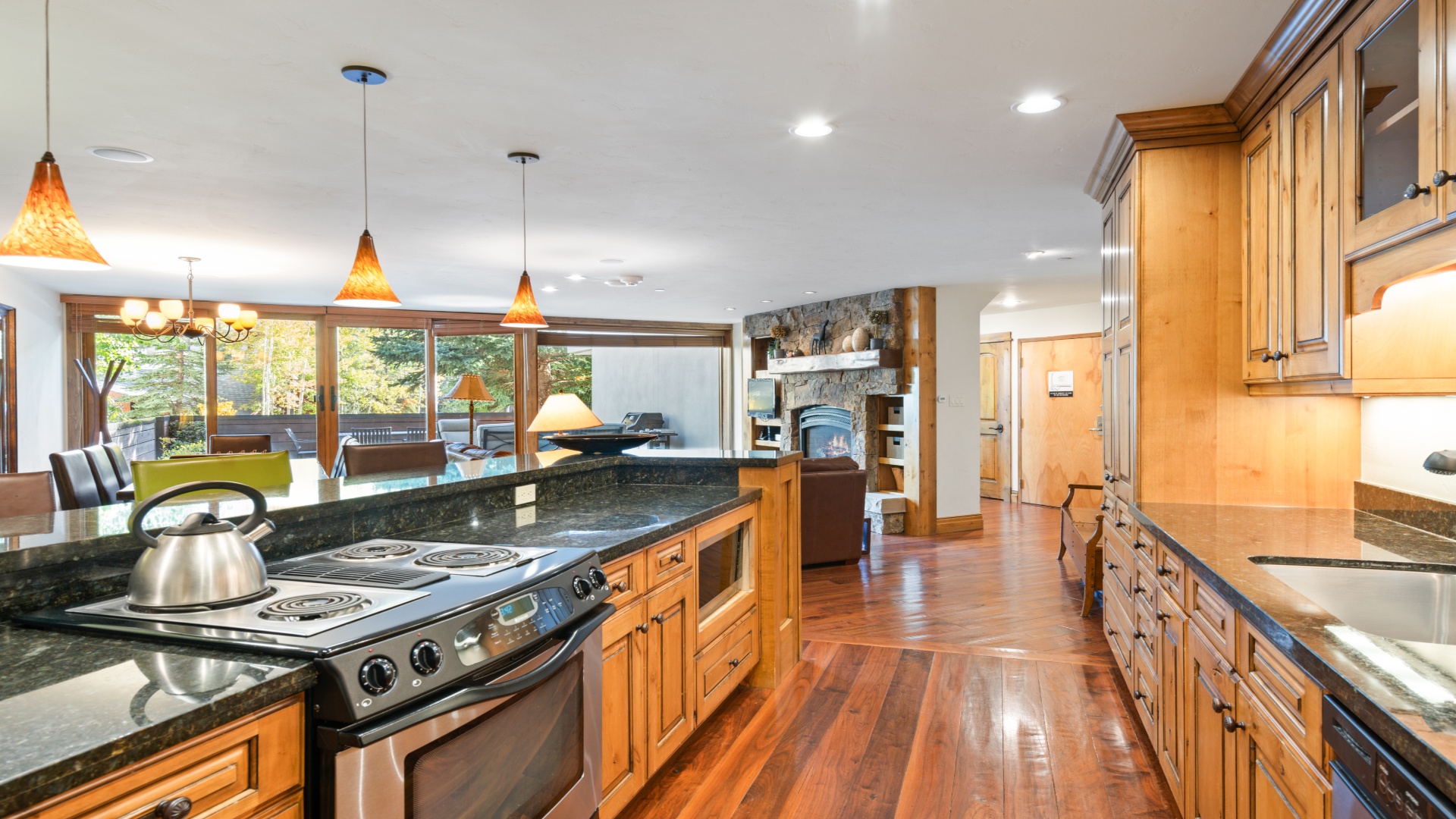 Step into your gourmet kitchen where rich wood cabinetry, gleaming granite counters, and a spacious island invite you to cook and gather. Natural light pours through expansive windows framing forest views.
