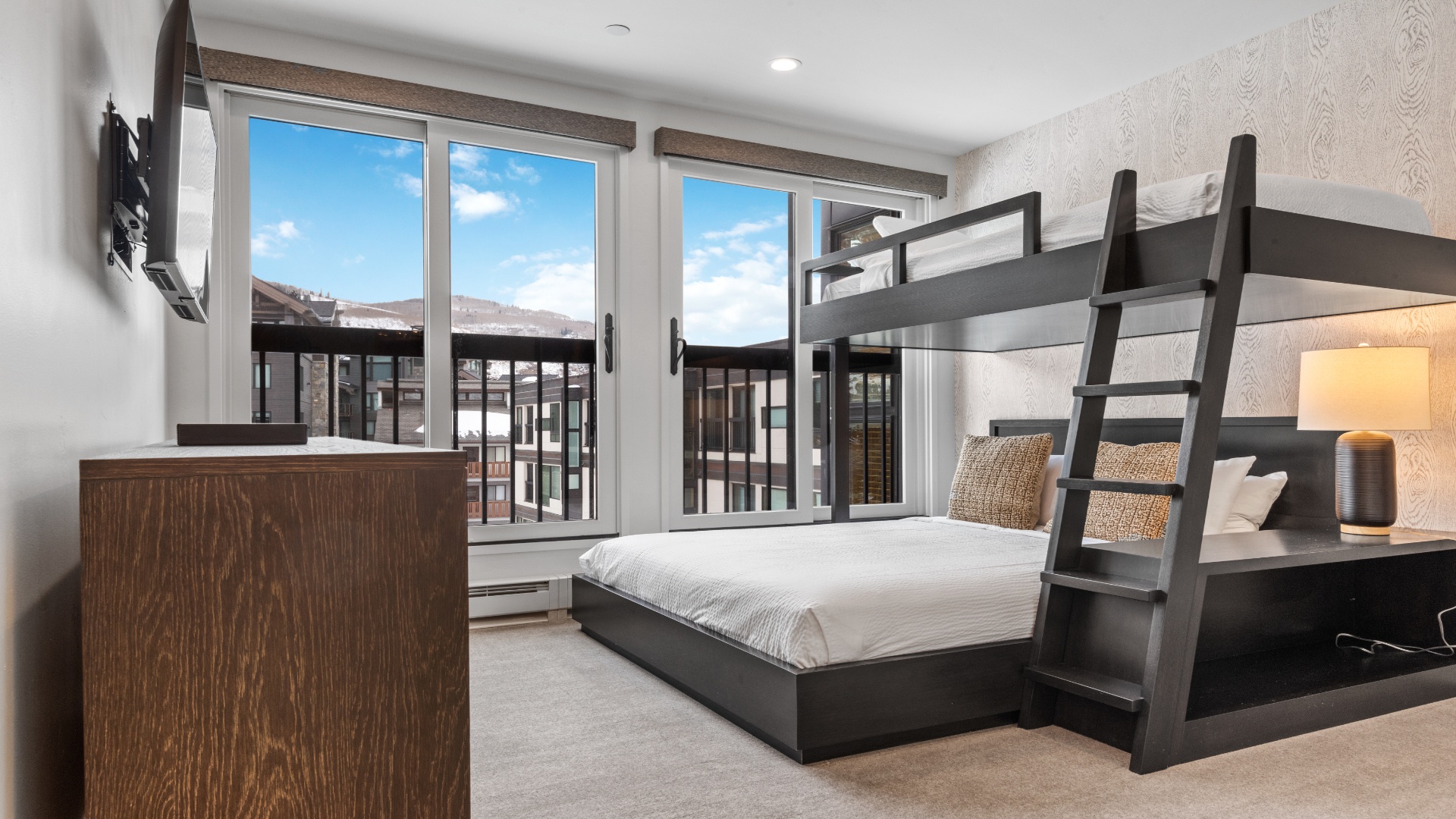 Your mountain-view bedroom features a cozy queen bed and bunk bed—perfect for families or groups. Natural light floods in through large windows overlooking the scenic landscape.