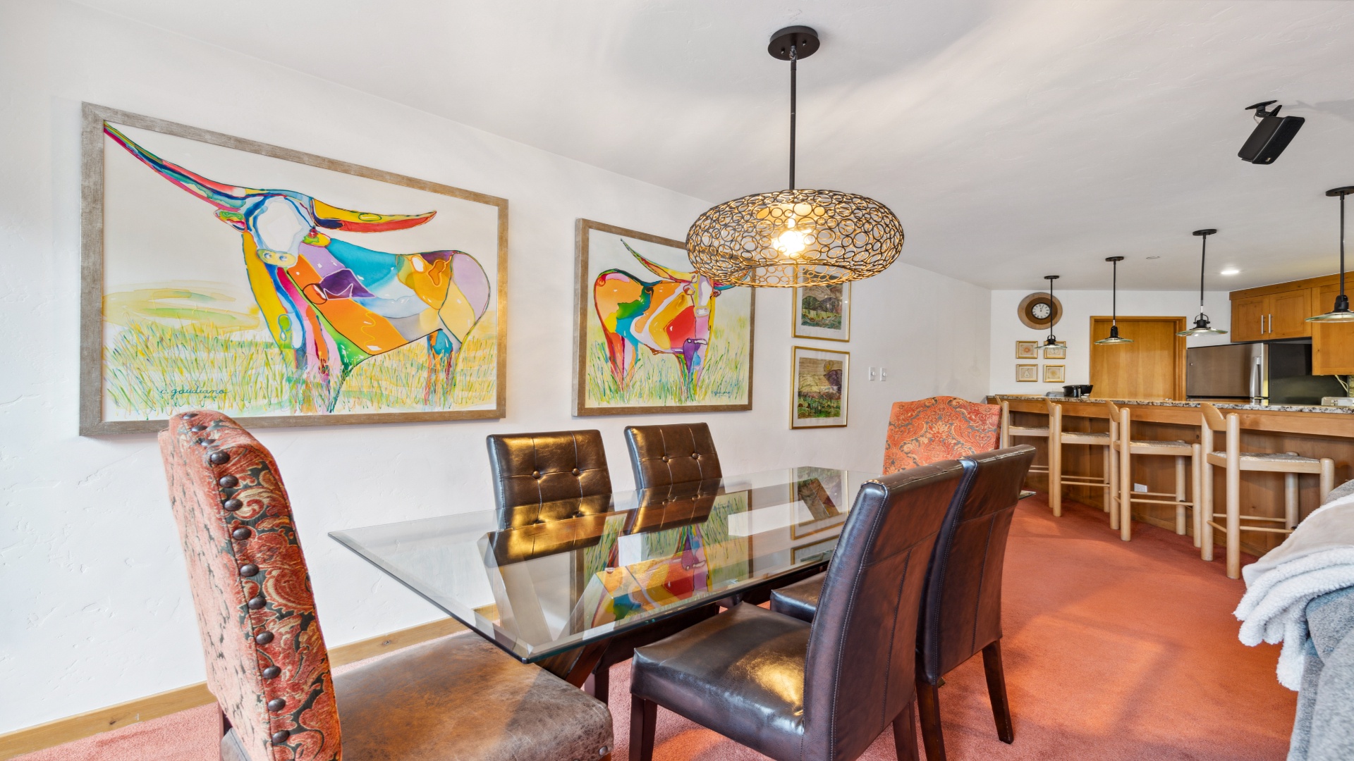 Gather around your spacious dining table beneath a stunning pendant light, where vibrant art and warm wood tones create a welcoming space for memorable meals together.