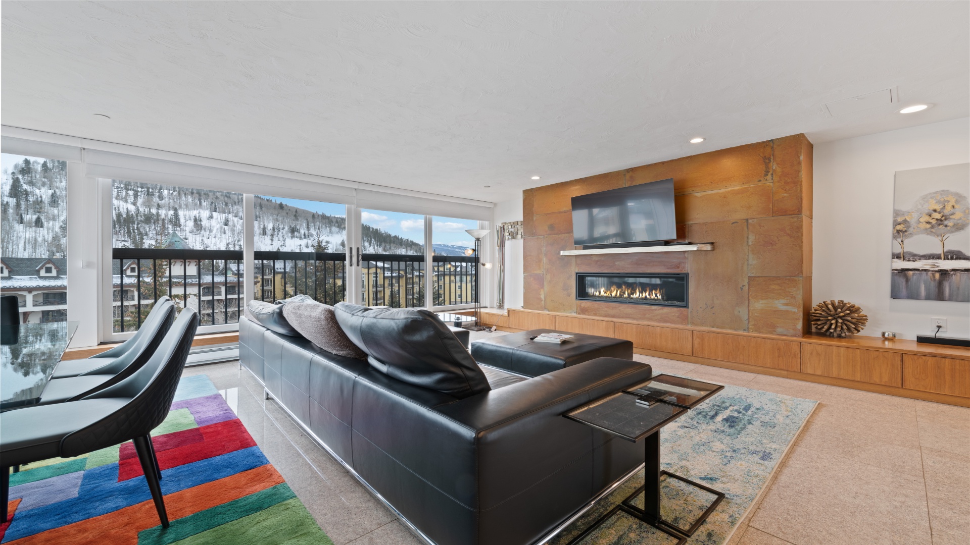 Unwind in your sleek living space where floor-to-ceiling windows frame stunning snowy mountain views, and the modern fireplace creates warmth and ambiance for cozy evenings after adventure-filled days.