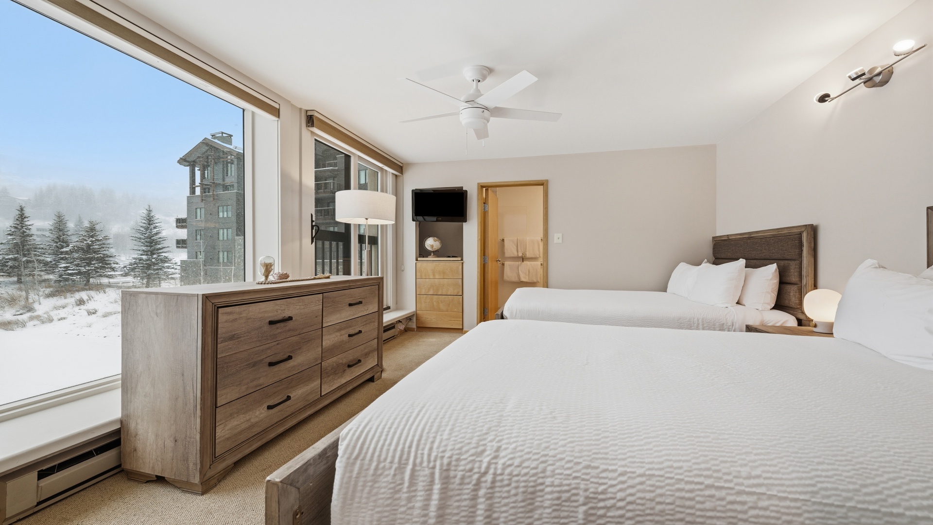 Two plush beds await you in this serene retreat, where floor-to-ceiling windows frame snowy mountain views. Warm wood tones and crisp white linens invite total relaxation after your alpine adventures.