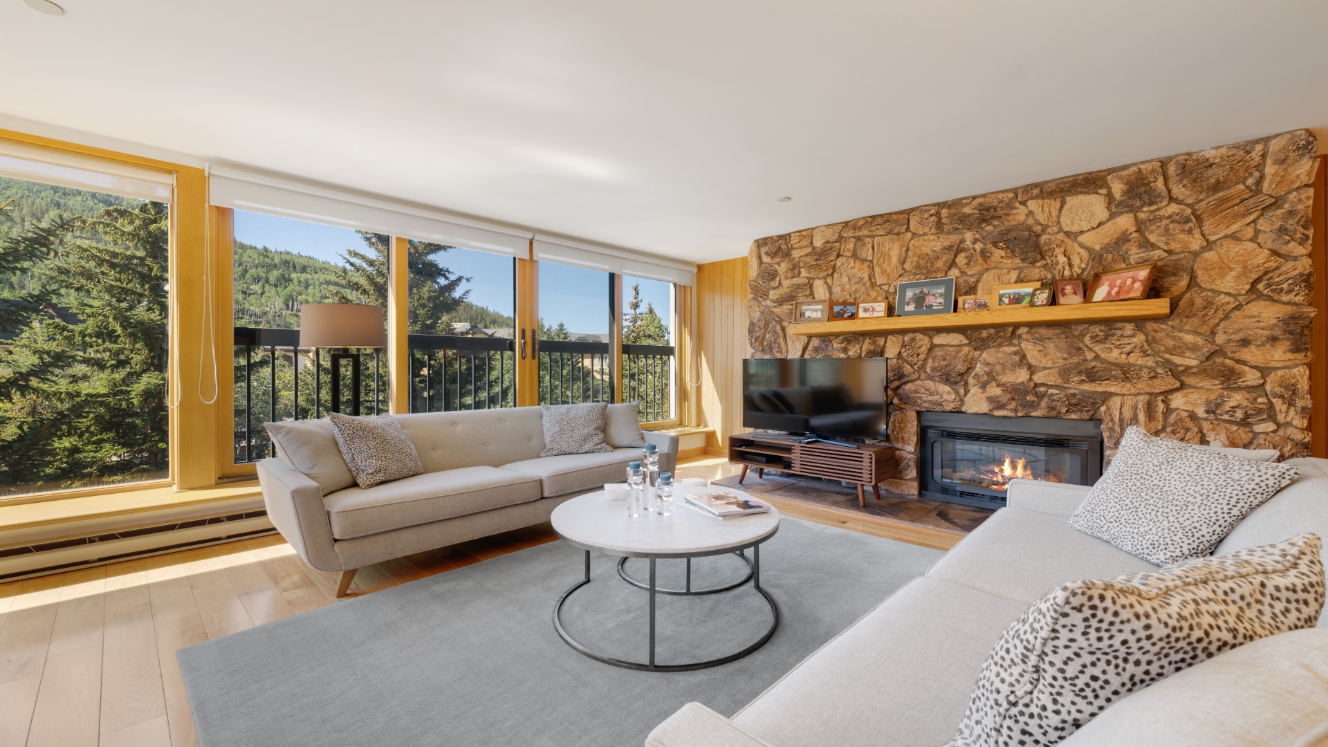 Unwind in your bright, spacious living room with a cozy stone fireplace, panoramic forest views, and plush seating perfect for relaxing after a day of adventure.