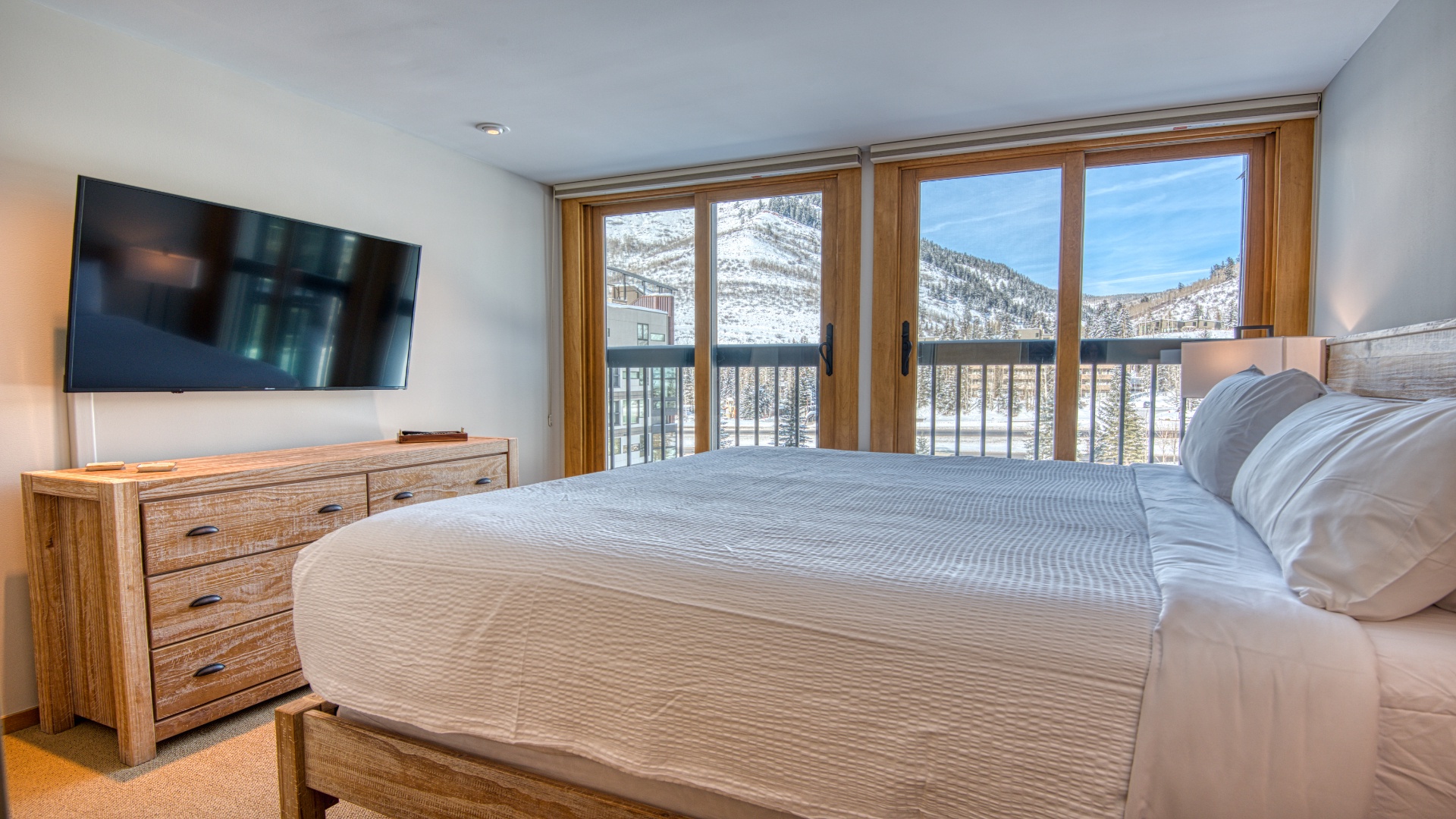 Wake up to breathtaking snow-capped mountain views framed by your private balcony. This serene bedroom blends rustic wood accents with modern comfort, inviting you to unwind in style.