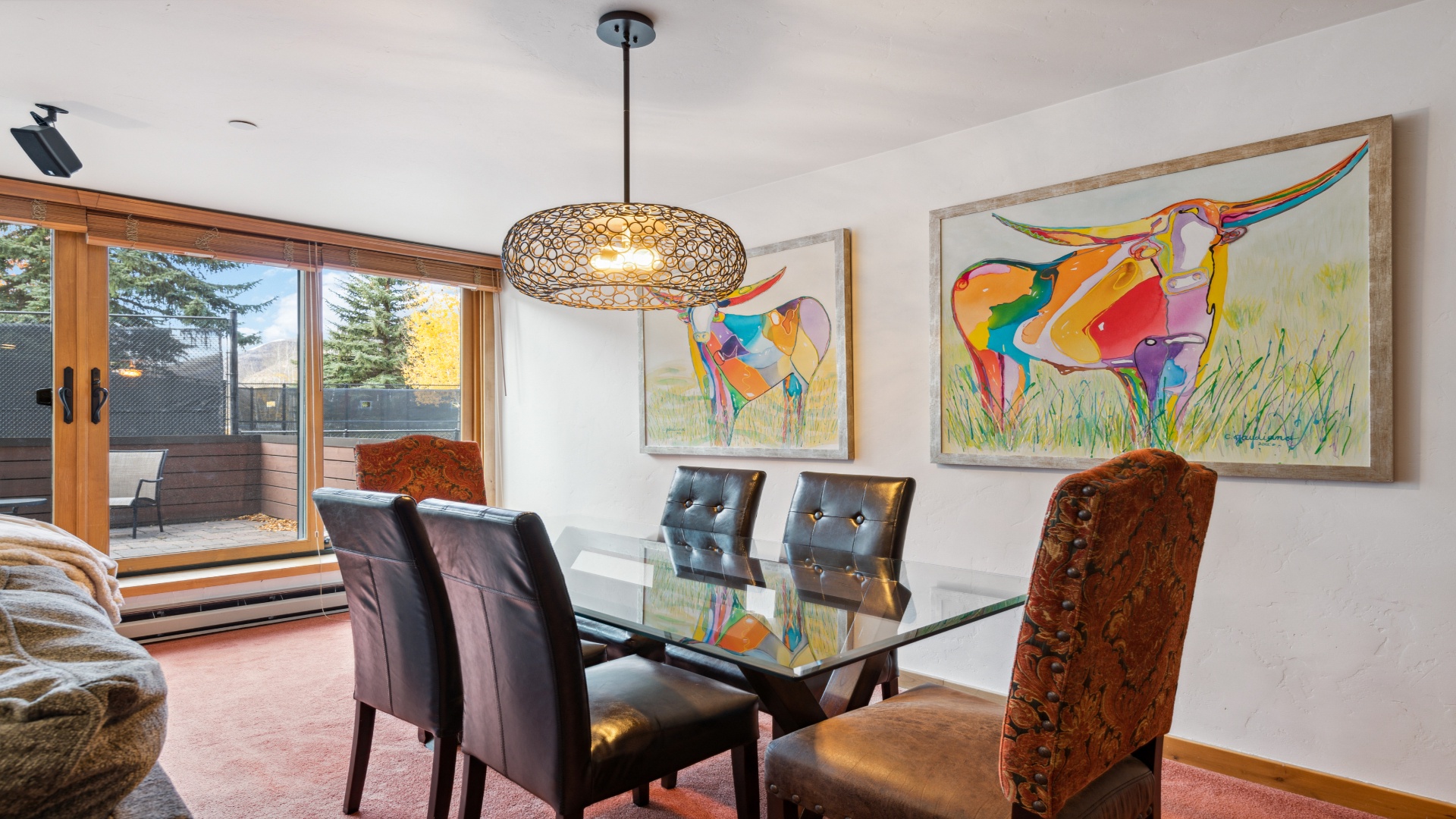 Gather around the glass-top table beneath a statement pendant light, where vibrant longhorn art adds personality to your meals and colorful outdoor views inspire mountain relaxation.