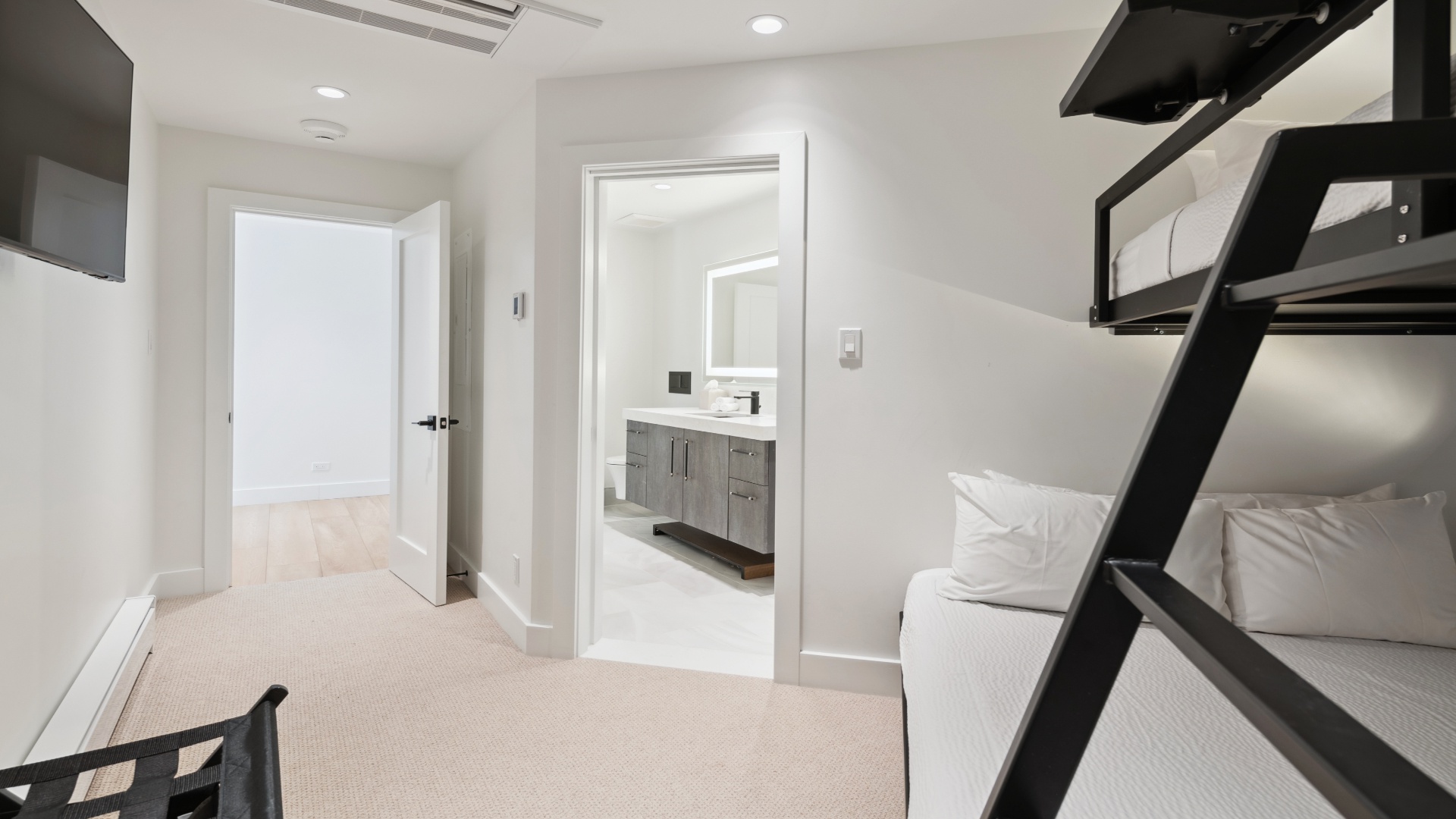 Climb into your bunk bed for a cozy night's sleep in this bright, modern bedroom with sleek black bunks, plush white linens, and an ensuite bathroom just steps away.