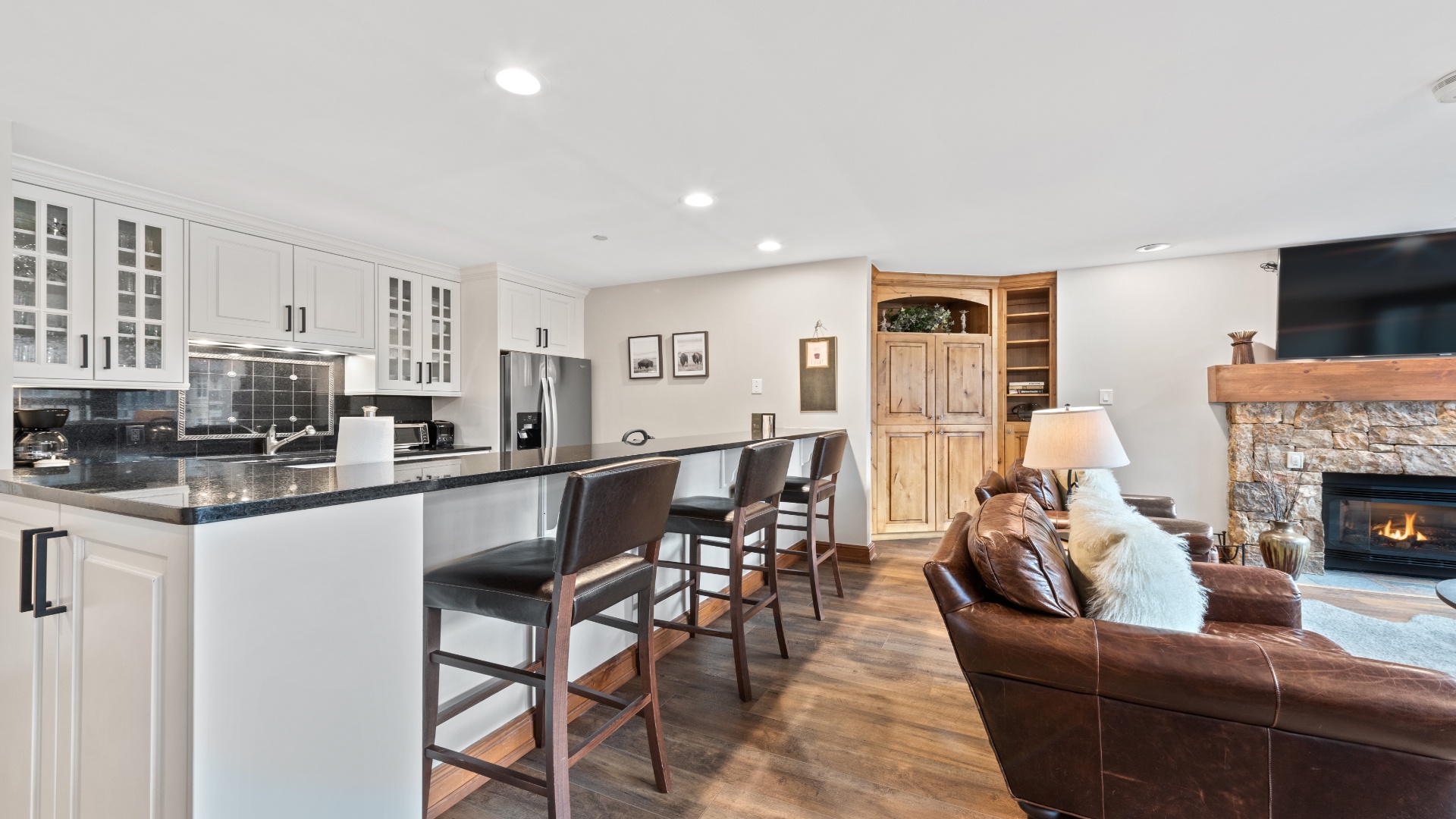 You'll love gathering in this open-concept living space where the sleek kitchen flows seamlessly into a cozy living area. Prepare meals at the granite-topped island, then unwind by the warm glow of the stone fireplace.