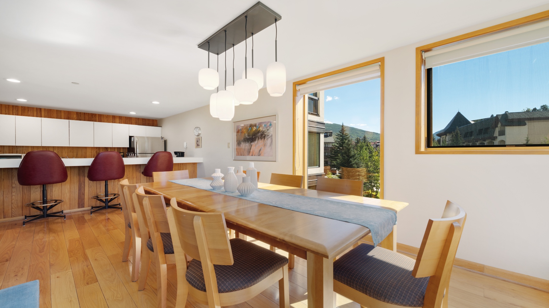 Gather around this spacious dining table where warm wood tones meet modern comfort, with mountain views framing your meals and a bright kitchen ready for your culinary adventures.