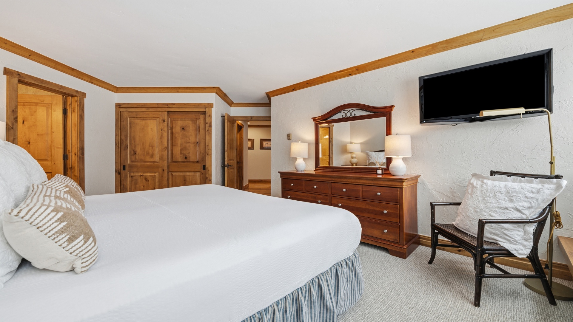 Your spacious bedroom features a plush bed, elegant wood furnishings, a wall-mounted TV, and a cozy chair—perfect for unwinding after a day of adventure.