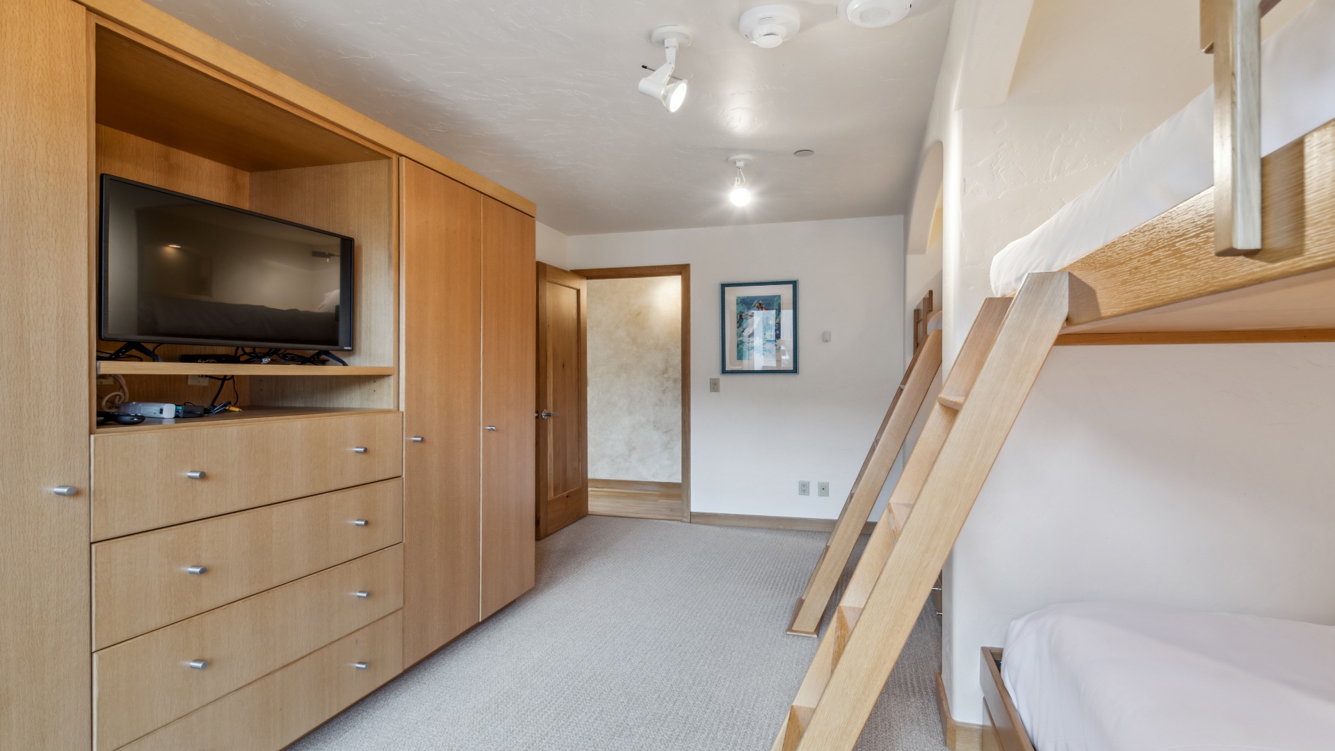 Your spacious bedroom features warm wood furnishings, including built-in storage, a flat-screen TV, and a convenient loft-style sleeping area with a sturdy ladder—perfect for families or groups.