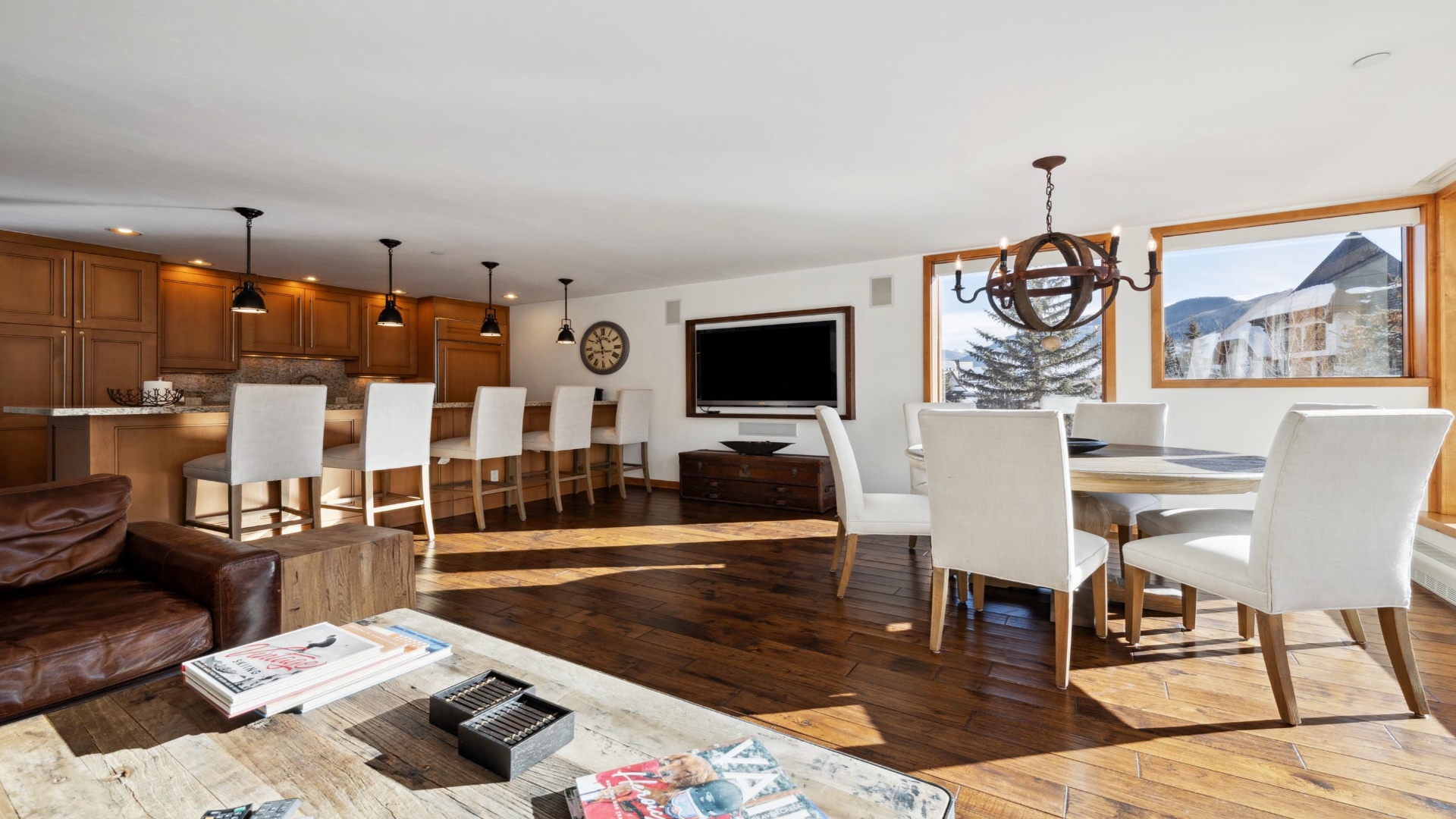 Sunlight streams through large windows framing mountain views, warming the rich hardwood floors of your open-concept living space where you'll gather around the dining table or unwind by the leather seating.
