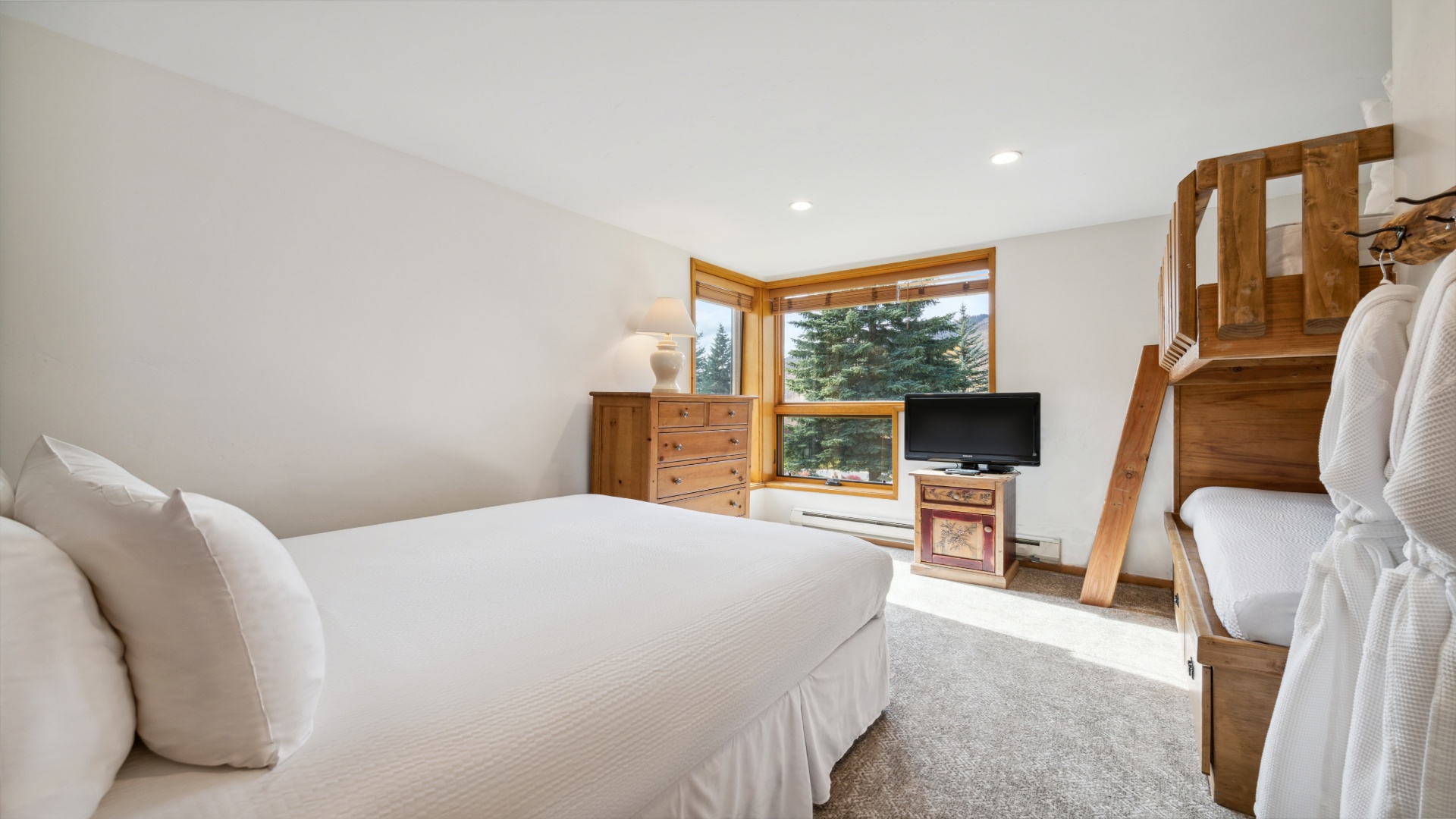 Drift off surrounded by crisp white linens and soft natural light, with evergreens framed outside your window and a cozy loft above for extra sleeping space.