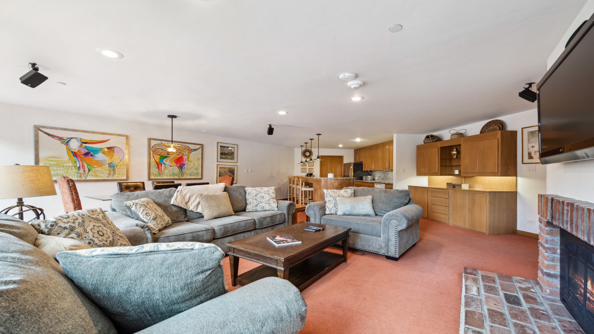 Relax in your spacious open-plan living area with plush sofas and vibrant art. The full kitchen awaits your culinary creations, and the warm fireplace sets the perfect cozy ambiance.