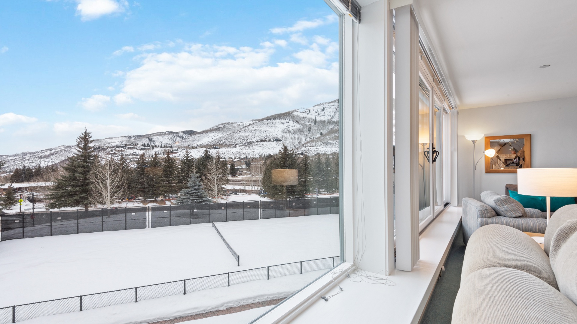 This peaceful bedroom features expansive windows framing snow-capped mountains and evergreen forests, with a cozy seating area bathed in natural light where you can unwind and soak in the alpine beauty.