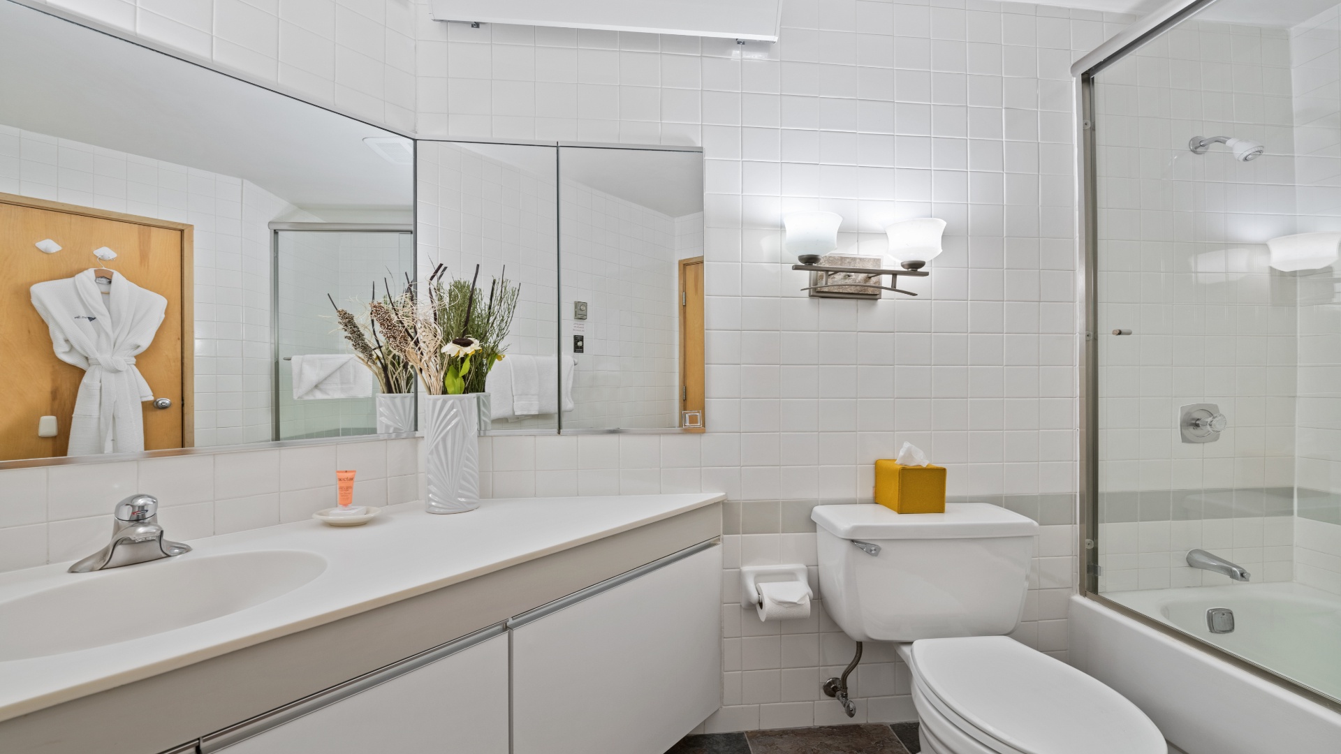 Your private bathroom features clean white tile, plush robes, a sleek vanity, and a shower-tub combo—perfect for unwinding after exploring the city.