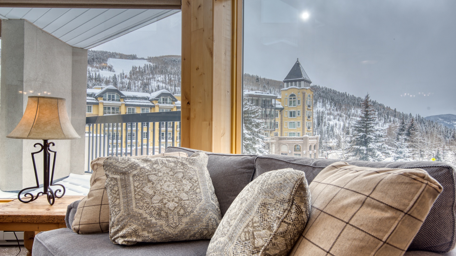 Relax in your cozy living space while enjoying breathtaking snow-dusted mountain views and charming alpine architecture through expansive windows that frame the winter wonderland outside.