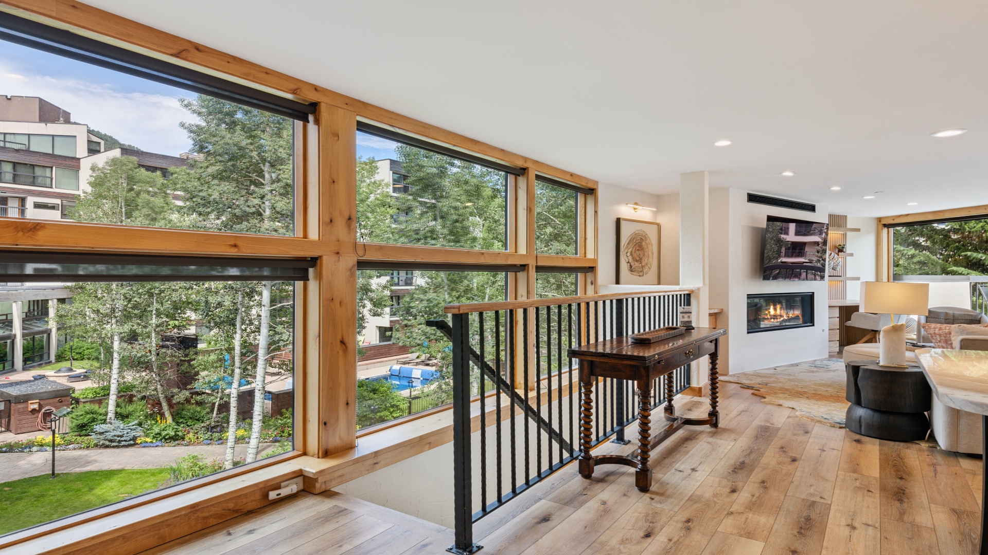 Modern living space with floor-to-ceiling windows framing leafy neighbourhood views. Warm wood beams and natural light create an airy, welcoming atmosphere throughout.