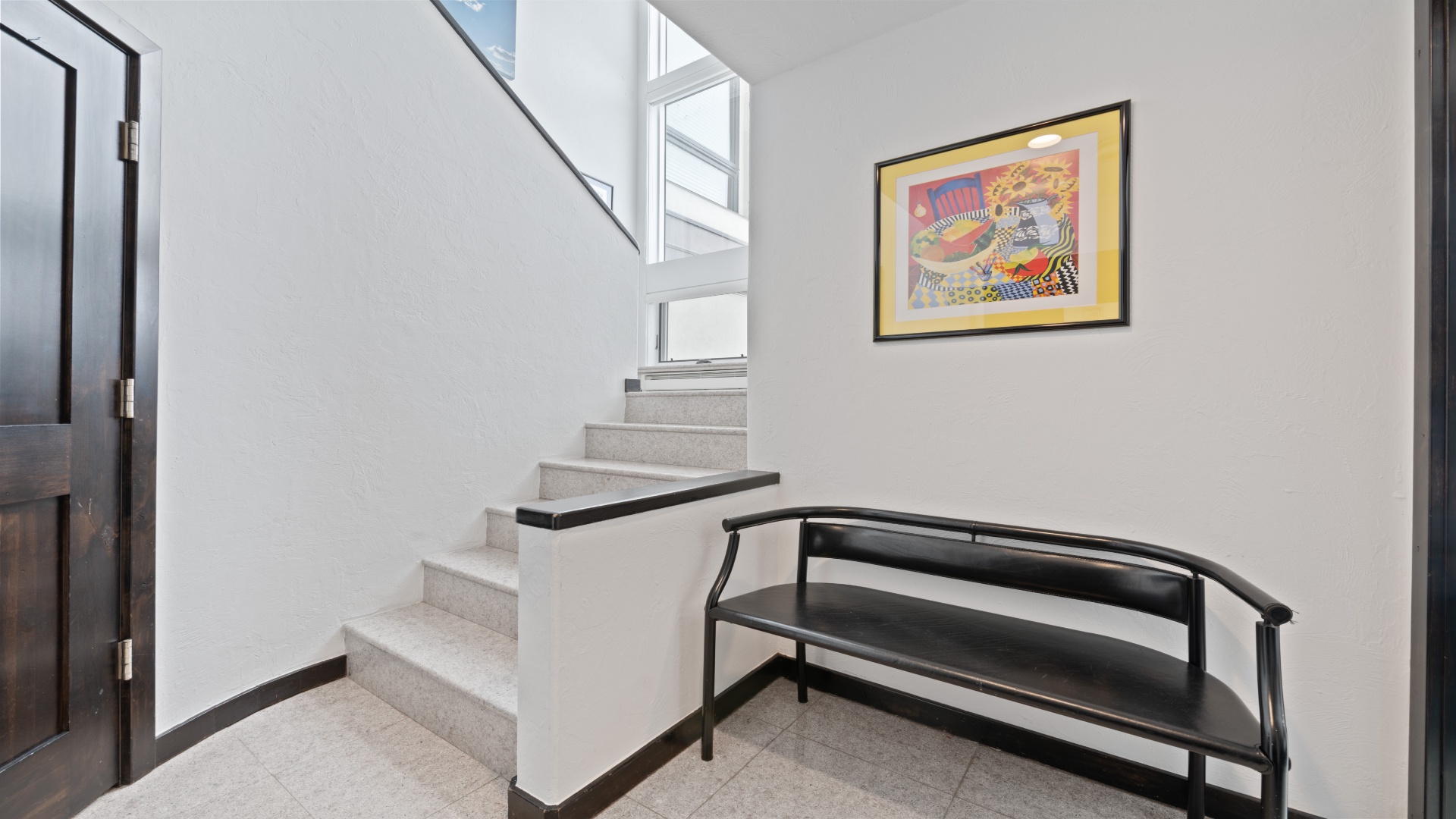 A bright, modern entryway features a welcoming staircase with sleek lines, a cozy bench to slip off your shoes, and cheerful artwork that instantly makes you feel at home.