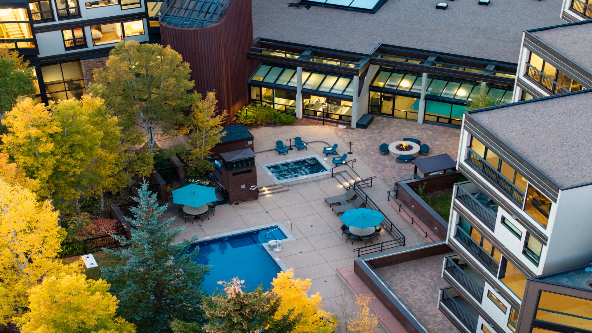 Aerial view of the property showcasing outdoor pool, hot tub, fire pit, and BBQ facilities surrounded by vibrant autumn foliage and modern multi-level buildings with private balconies.