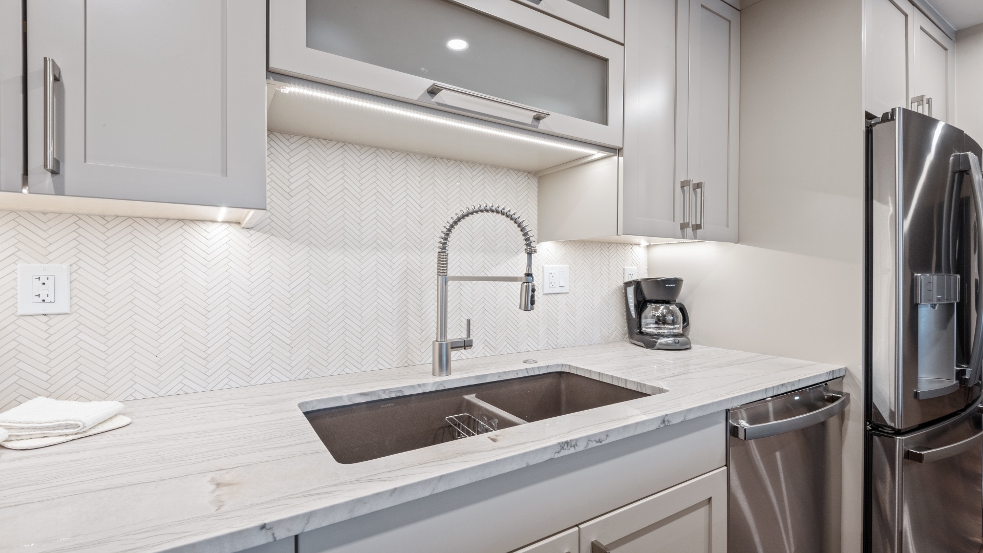A gleaming kitchen awaits you with polished counters, stainless steel appliances, and elegant herringbone tile backsplash—everything ready for your morning coffee or a leisurely meal.