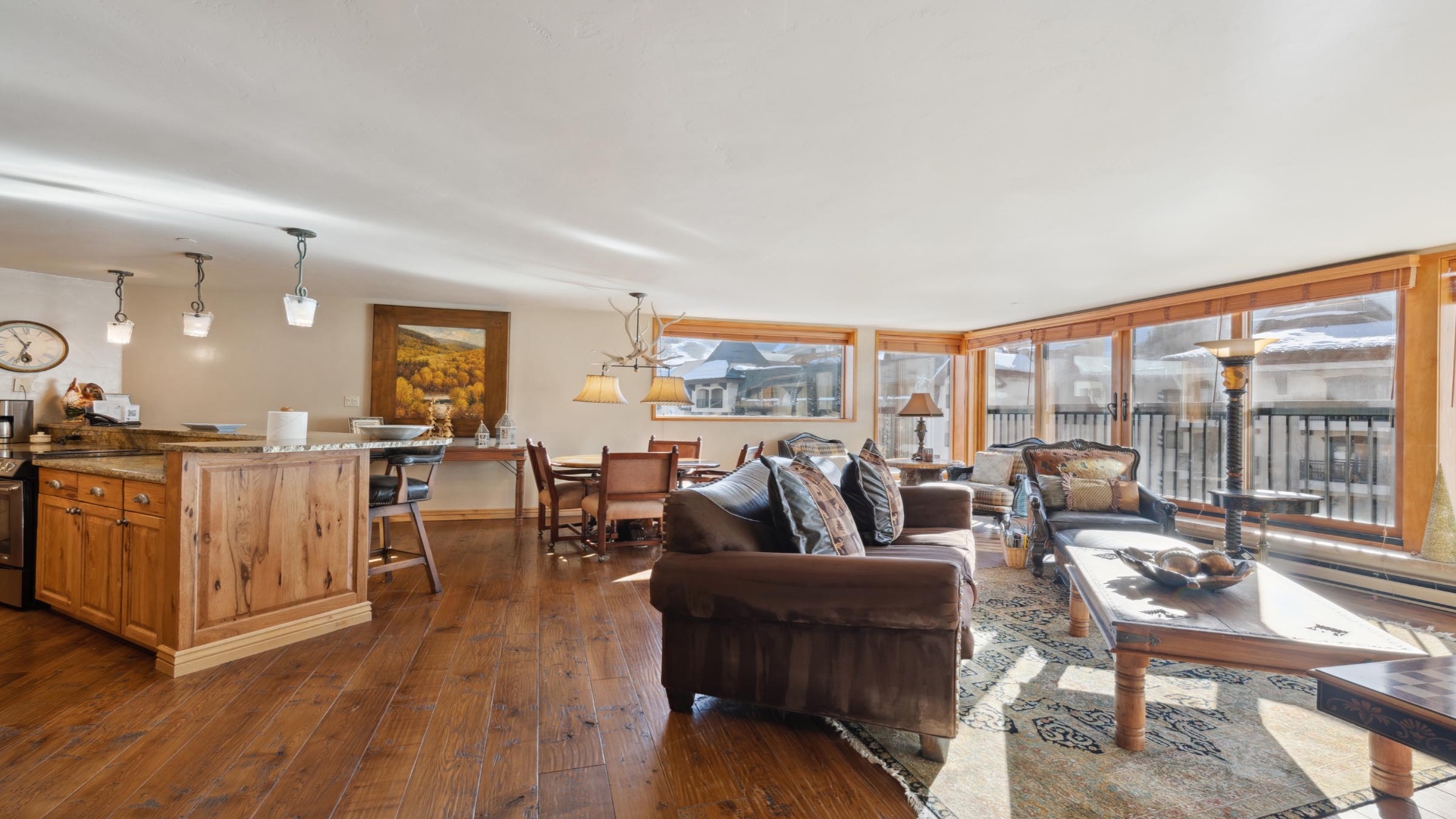 Sunlight floods through expansive windows, warming rich wood tones and plush leather sofas in this open-concept living space where mountain air and cozy gatherings await you.