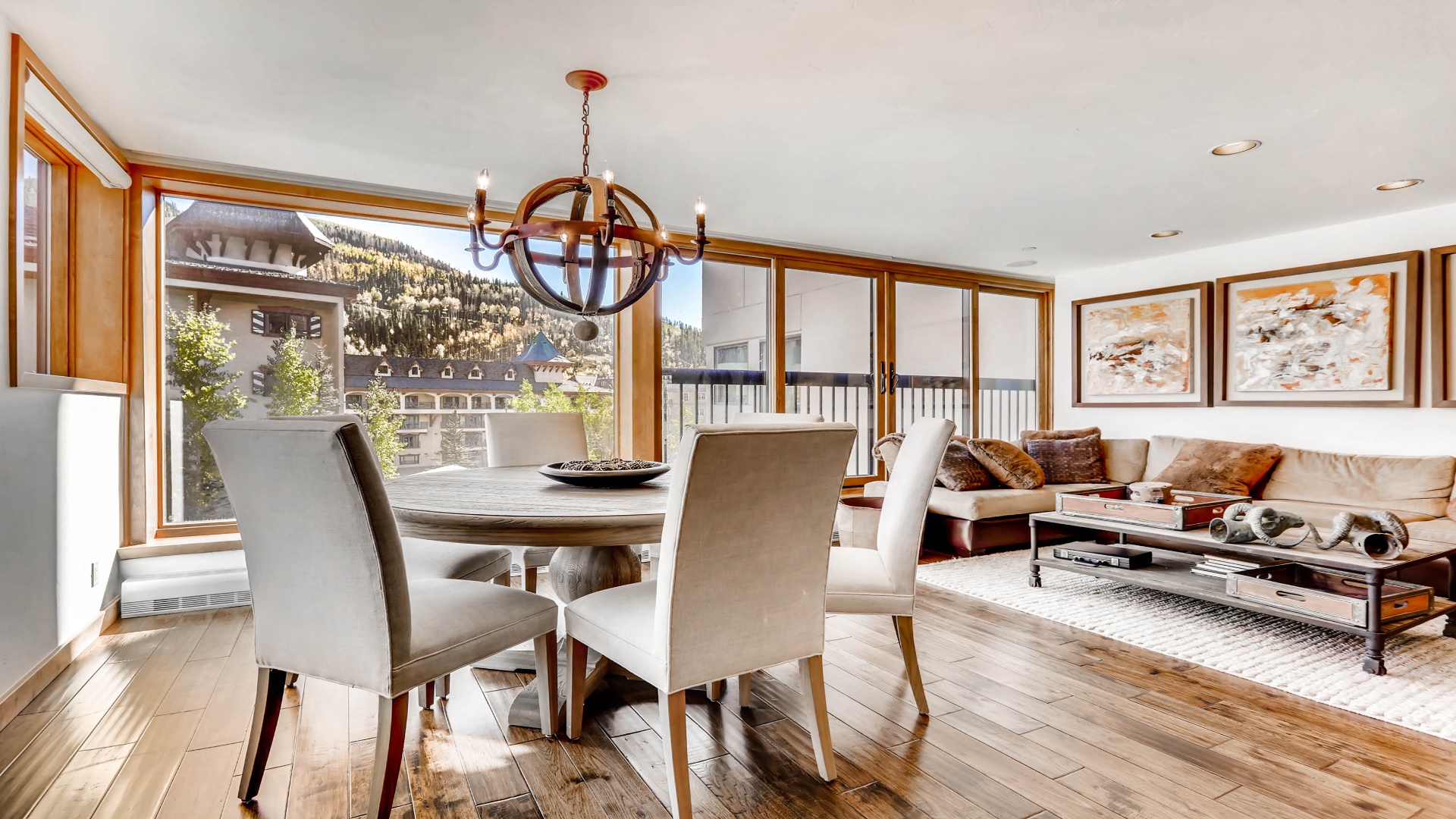 Picture yourself sharing meals at this elegant round dining table, natural light streaming through floor-to-ceiling windows framing mountain views, then relaxing in the adjacent living area with cozy throws and a warm, inviting atmosphere.