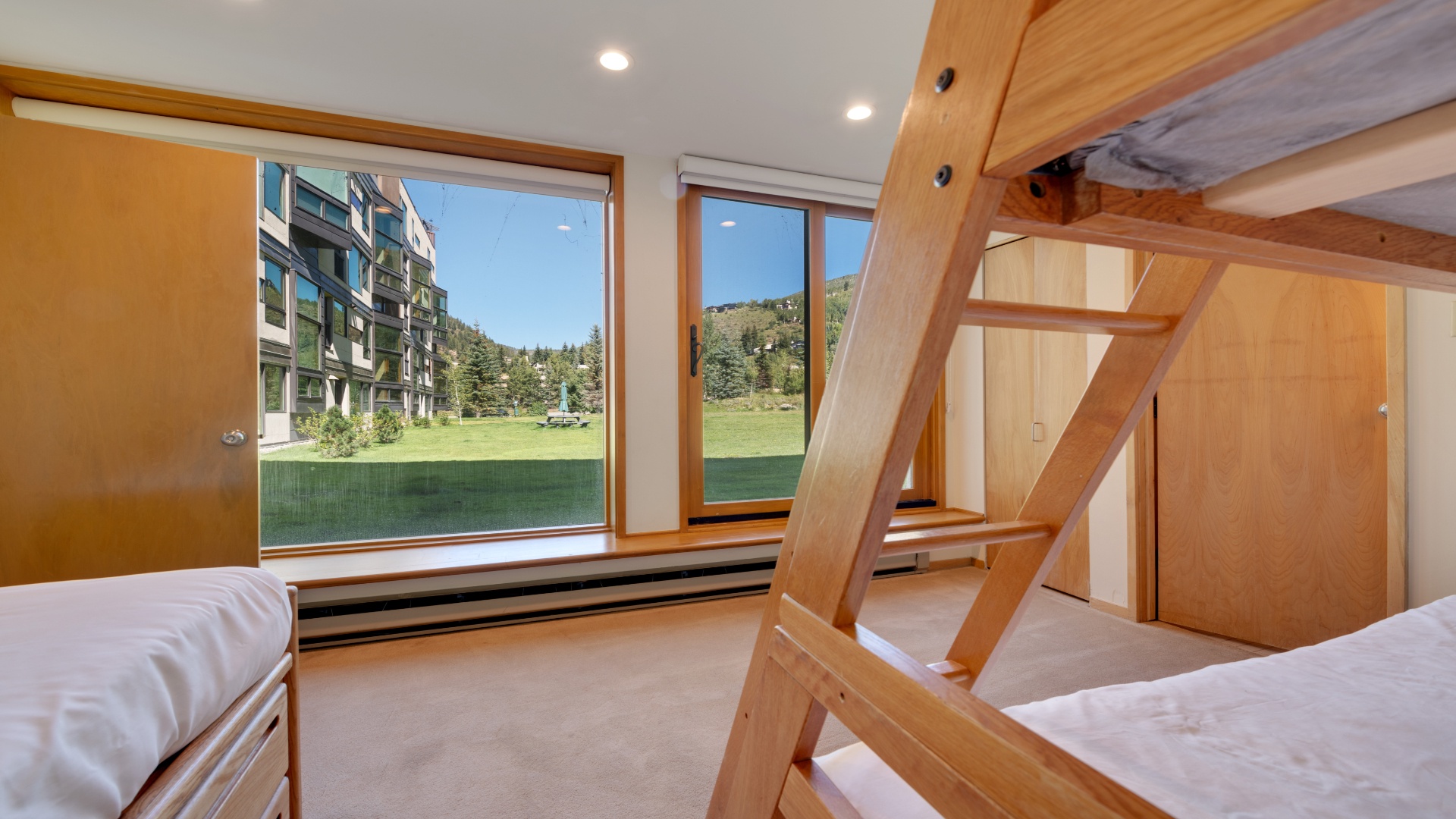 Your room features a bunk bed and large windows framing lush green lawns and mountain scenery, creating a cozy retreat with natural light and peaceful views.