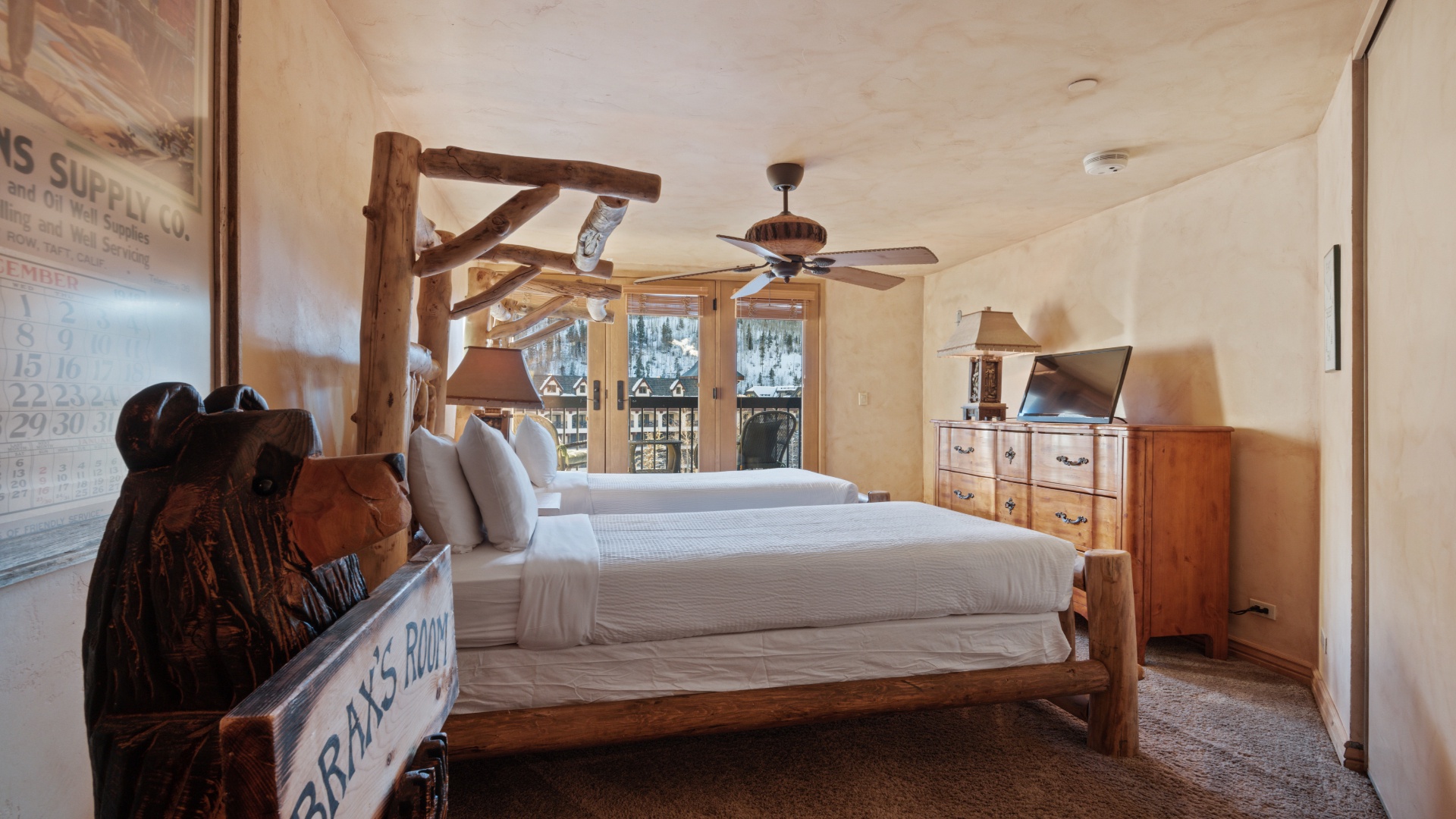 Step into your cozy alpine retreat where rustic log beds and warm wood tones create a charming mountain escape, with peaceful snowy views just beyond your balcony doors.
