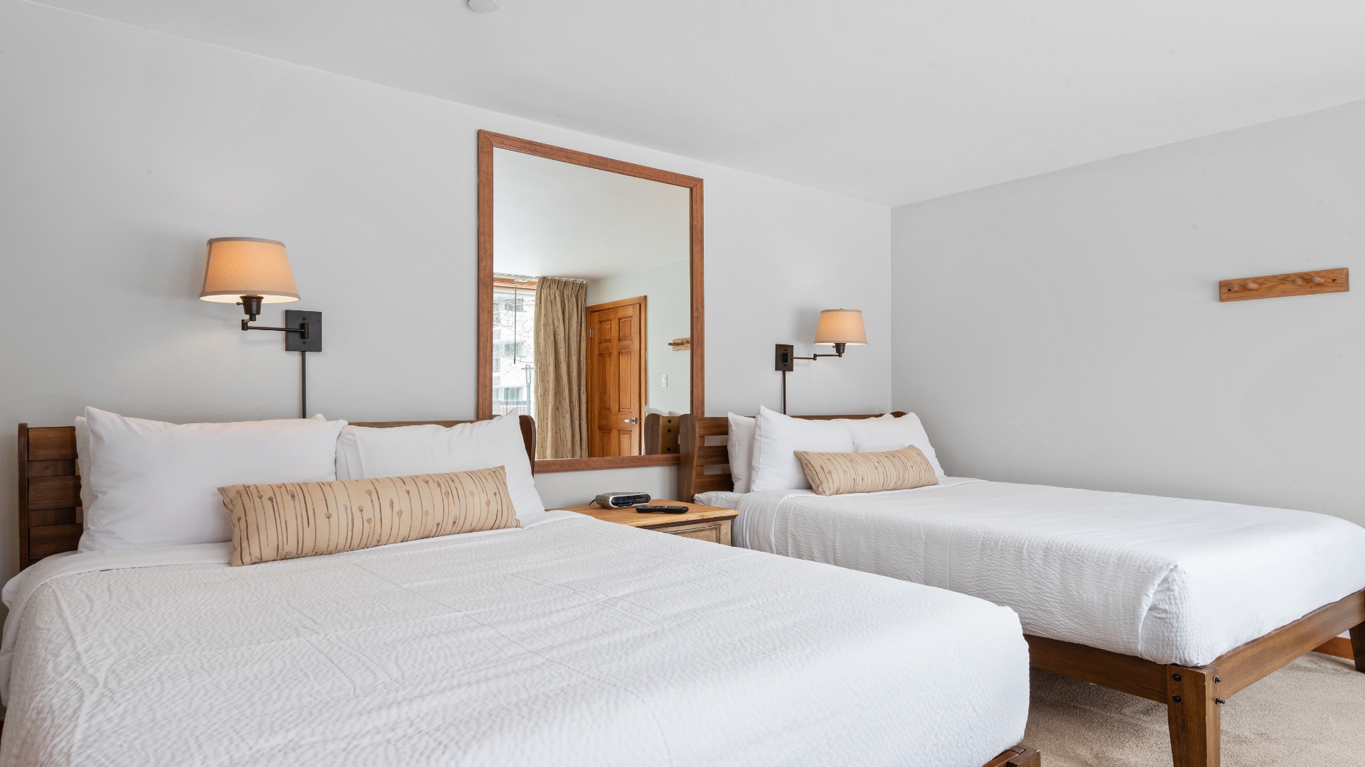Two inviting queen beds with crisp linens and warm wood frames offer comfort after a day of adventure. Soft wall sconces and subtle textures create a serene retreat.