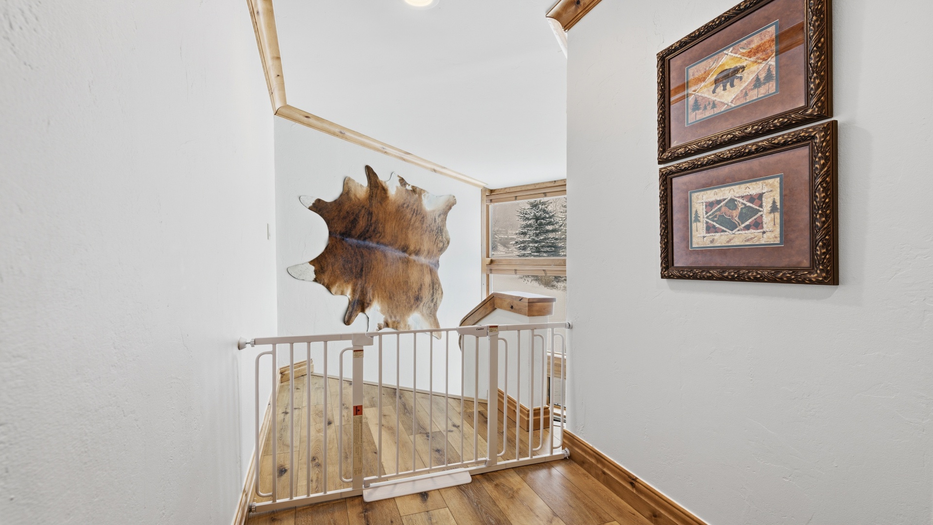 A rustic stairway adorned with cowhide and mountain-themed artwork leads you upward, while skylights above flood the space with natural light and glimpses of evergreens outside.