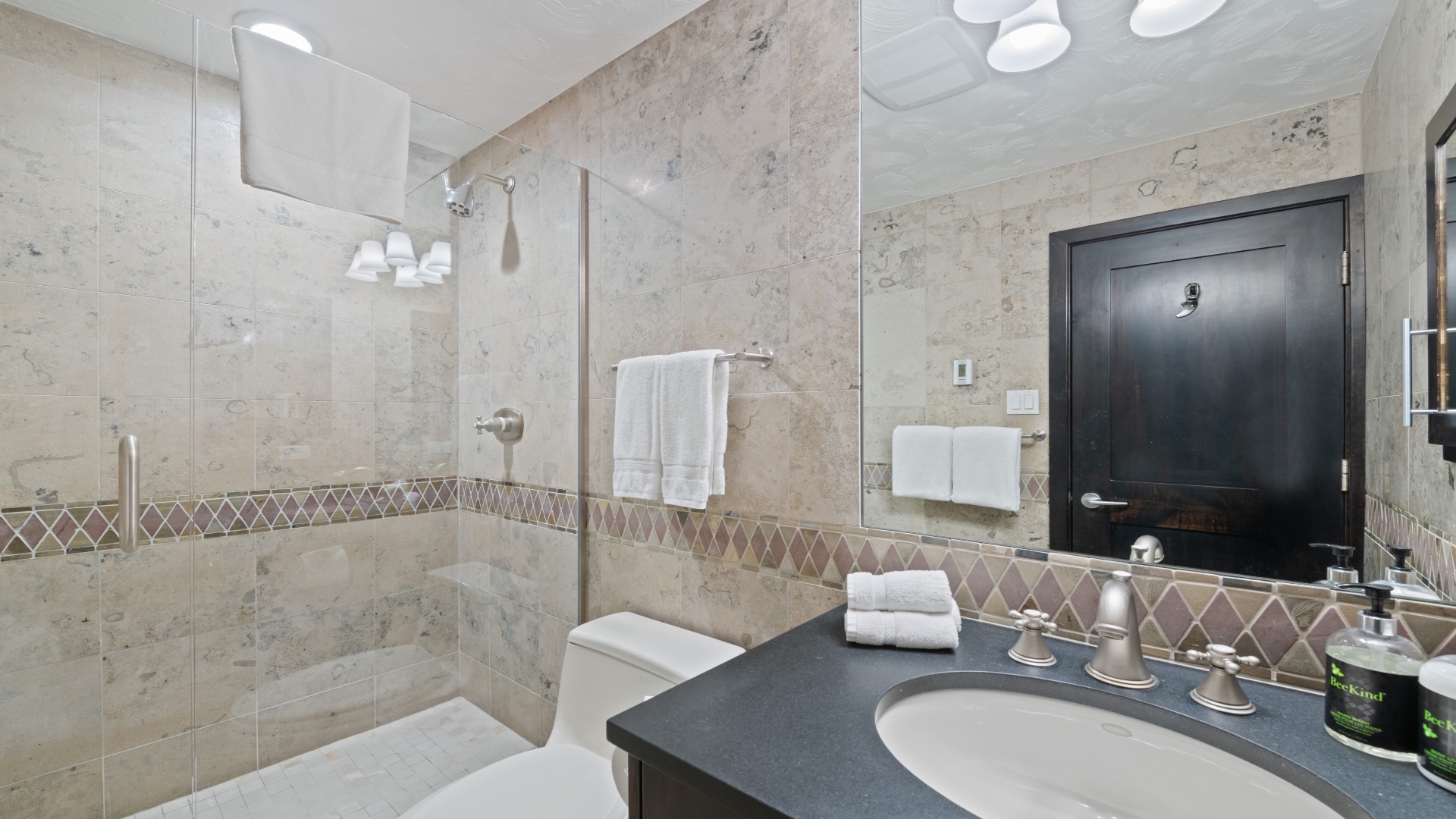 Your private bathroom features elegant travertine tile, a glass-enclosed shower, and plush white towels ready for you to unwind after a day of adventure.