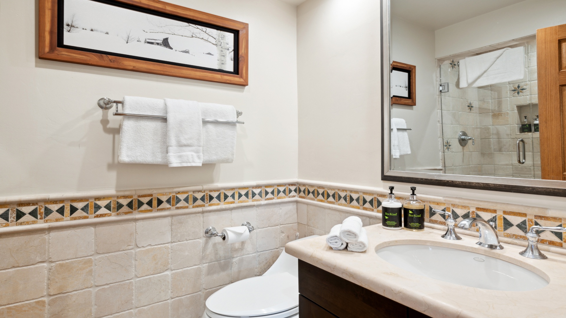 Freshen up in your bright, elegantly tiled bathroom with plush towels, a spacious vanity, and a glass-enclosed shower ready for your morning routine.