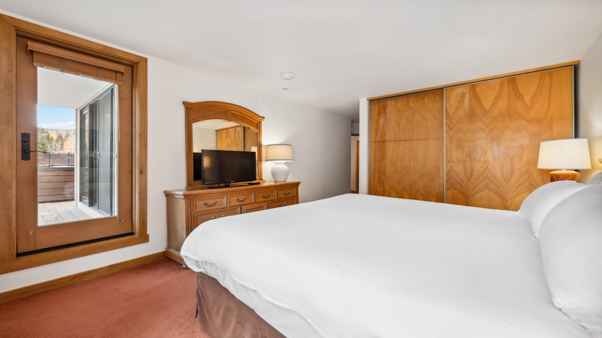 Sink into plush white linens and wake to mountain views through your private balcony door. This cozy bedroom blends warm wood tones with modern comfort, perfect for your restful mountain retreat.