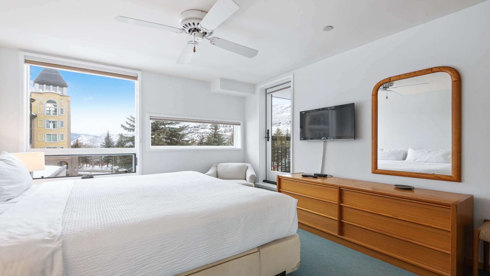 Drift off in this bright bedroom with your personal balcony and mountain views, where crisp white linens and a gentle ceiling fan create the perfect retreat after a day of adventure.