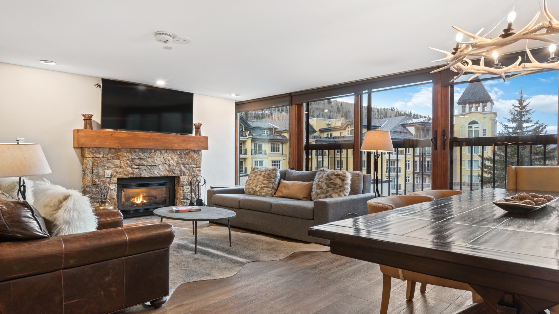Gather in your open-plan living area featuring a stone fireplace, mountain views, and rustic-chic decor perfect for après-ski relaxation.