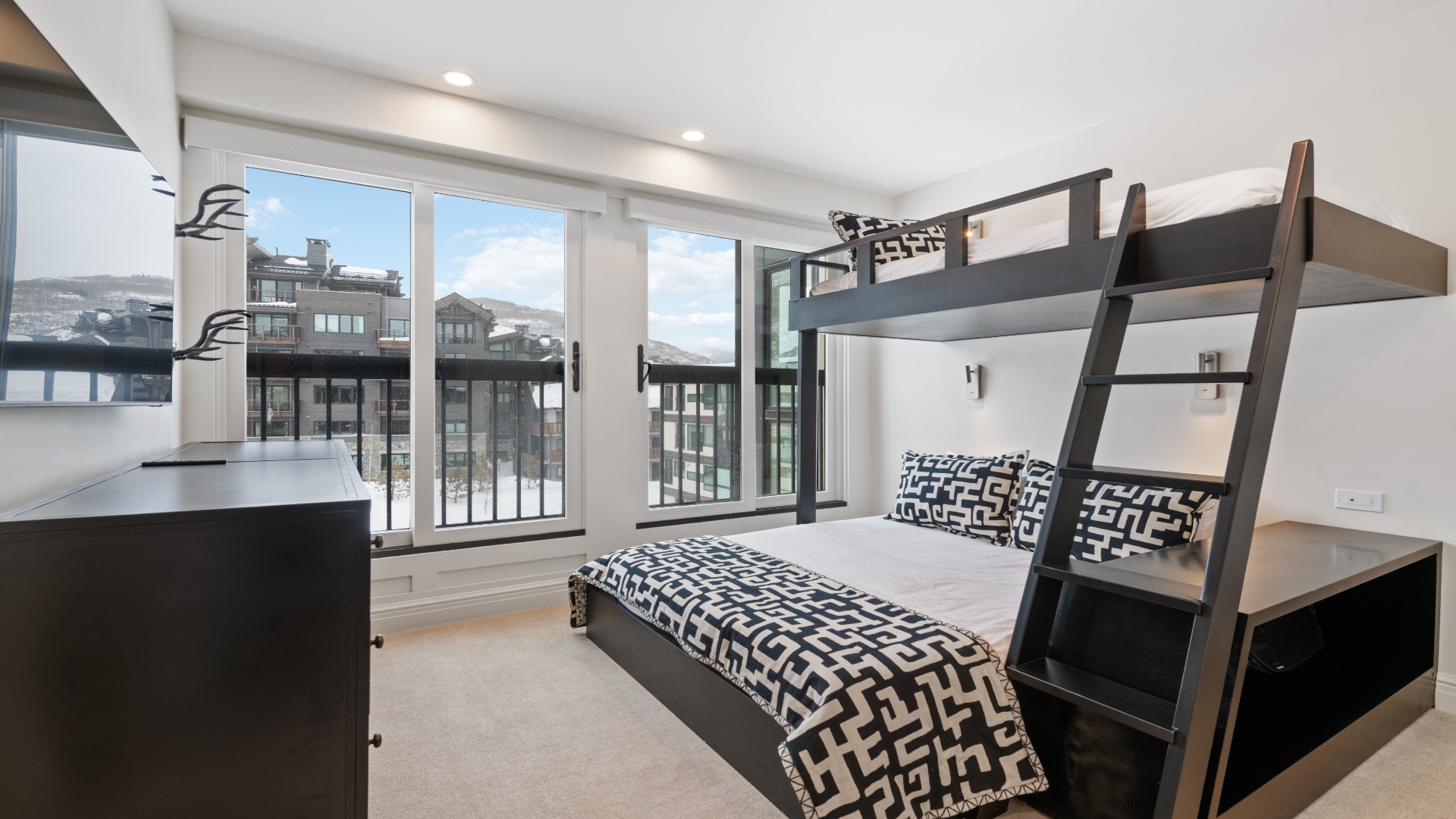 Your stylish bedroom features a modern bunk bed setup and sleeps multiple guests comfortably. Large windows frame mountain views, while fresh linens and thoughtful lighting create a cozy retreat for restful evenings.