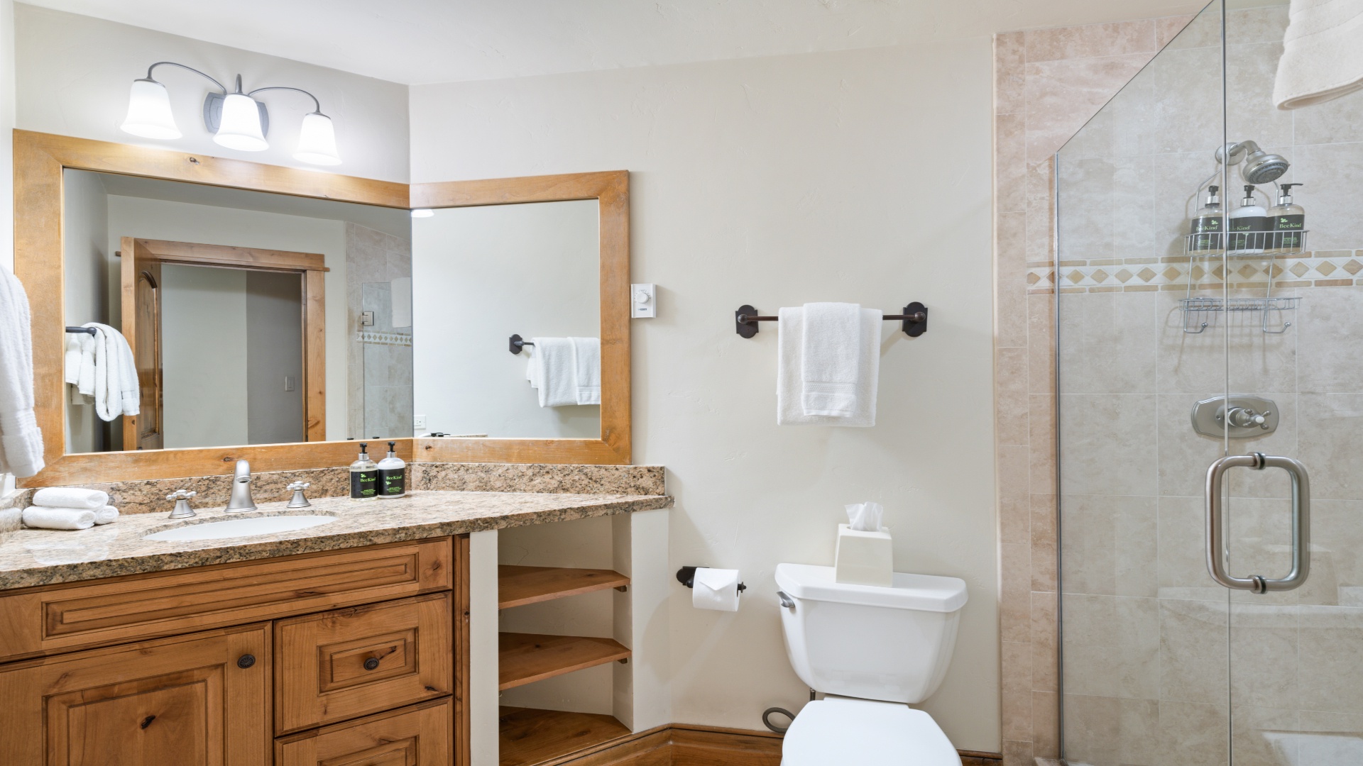 Your private bathroom features warm wood cabinetry, granite countertops, plush towels, and a glass-enclosed walk-in shower—everything you need to unwind after a day exploring.