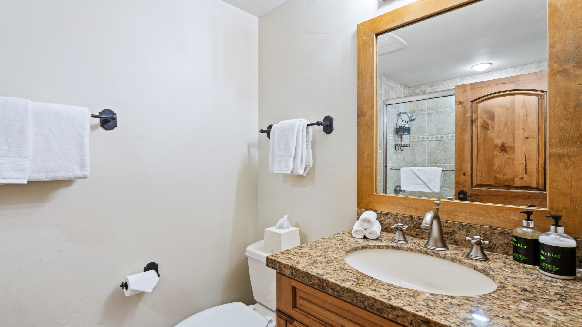 Relax in your private bathroom featuring granite countertops, rustic wooden cabinetry, plush white towels, and a beautifully tiled walk-in shower—designed for your comfort and convenience.