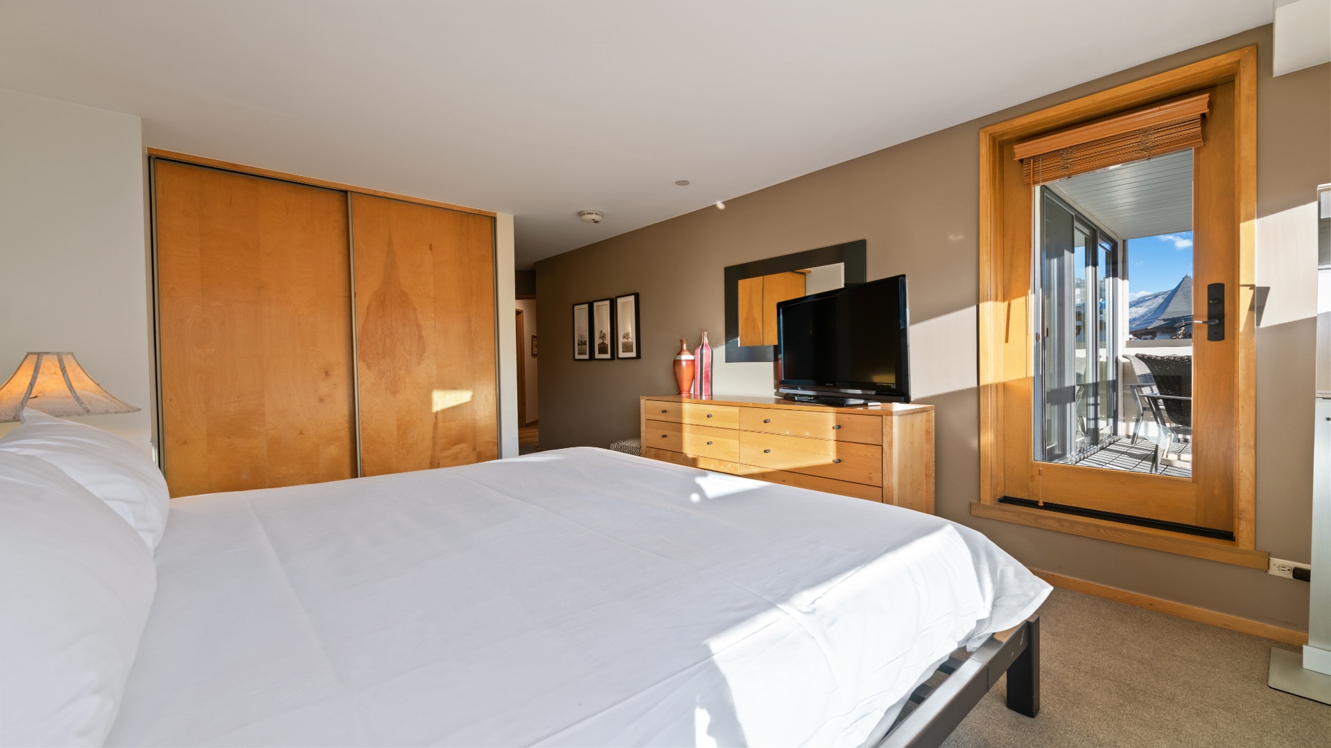 Sink into crisp white linens and wake to stunning mountain views through your private balcony doors. Natural wood tones and sunlight create a warm, restful retreat just for you.