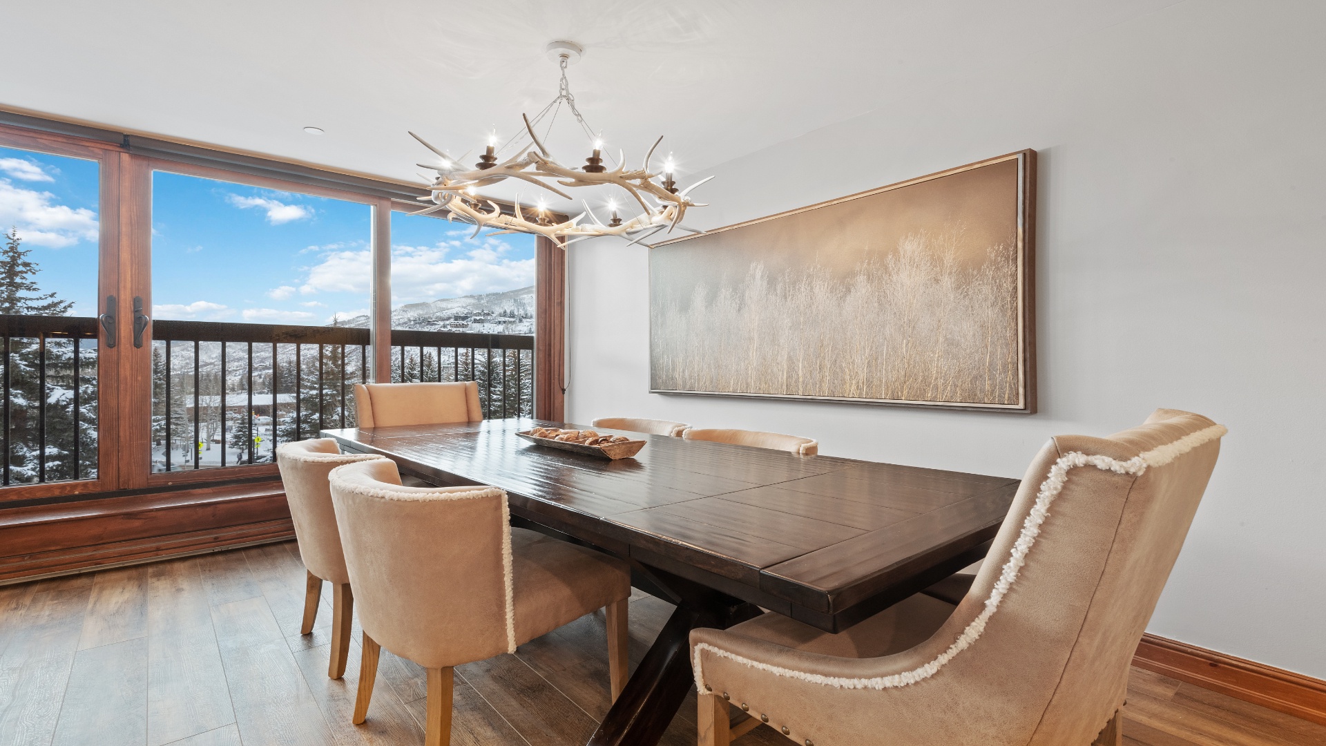 Gather around this elegant dining table with mountain views framing your meals. The rustic chandelier and natural tones create a warm, inviting space for memorable conversations.