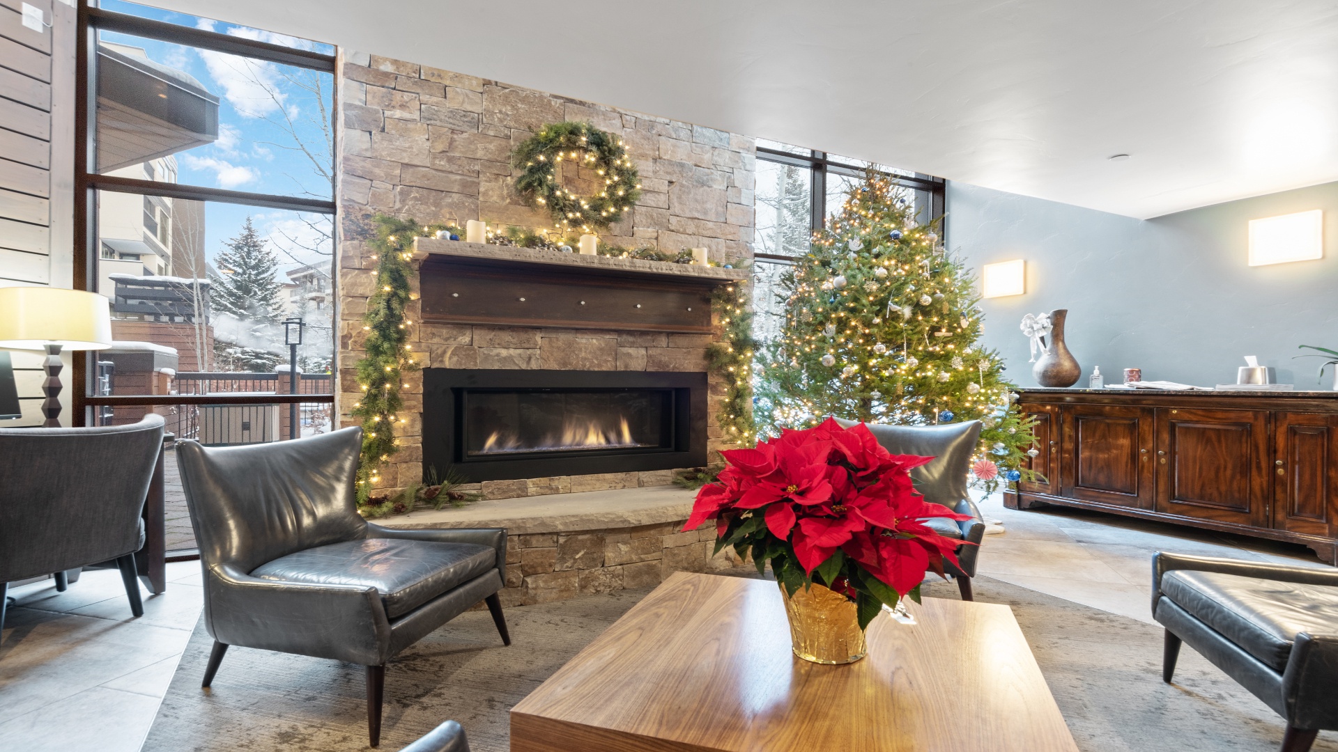 A festive stone fireplace glows warmly beside a beautifully lit tree, creating a cozy spot for your holiday retreat. Sink into plush seating and savor the seasonal charm.