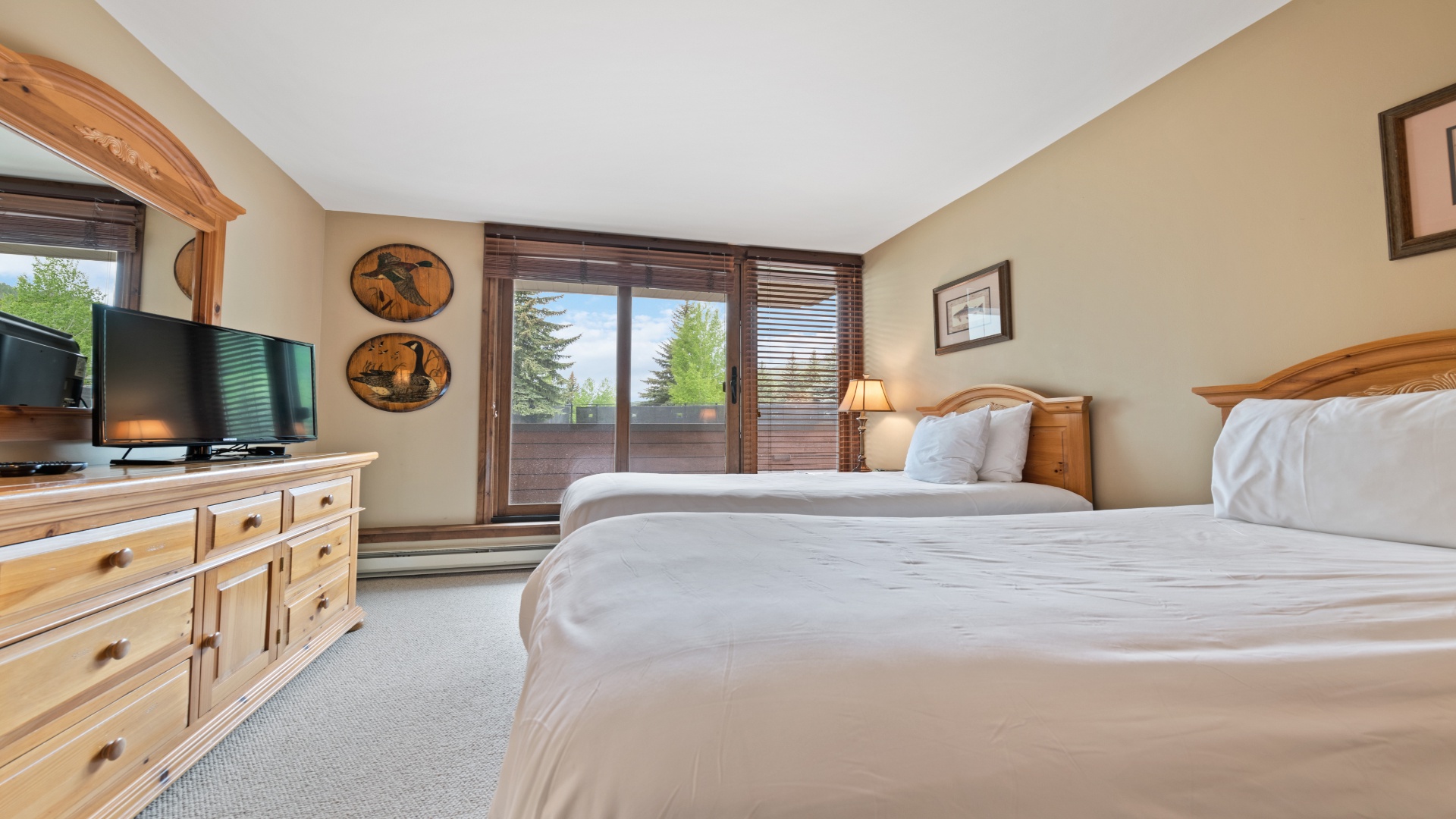 Sink into plush beds after a day of adventure. Natural light floods in through your private balcony door, framing trees and mountain air. Rustic wood accents and cozy touches make this space your perfect retreat.