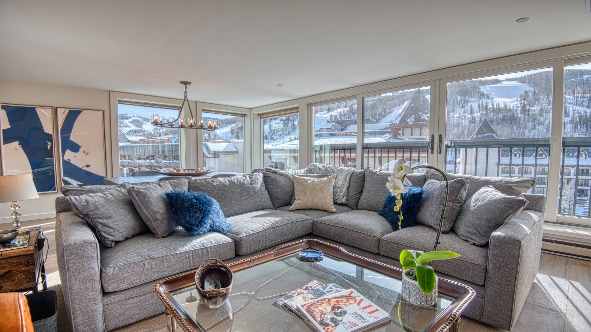 Stunning mountain resort views frame this spacious living room, where a plush sectional and thoughtful decor create the perfect après-ski retreat in a pristine winter setting.
